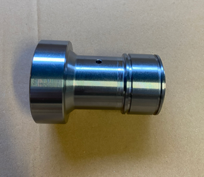 A shiny metallic machine part or component placed on a beige surface.