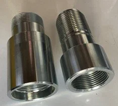 Two metallic threaded cylindrical objects, likely pipe fittings or adapters, placed side by side on a white surface.