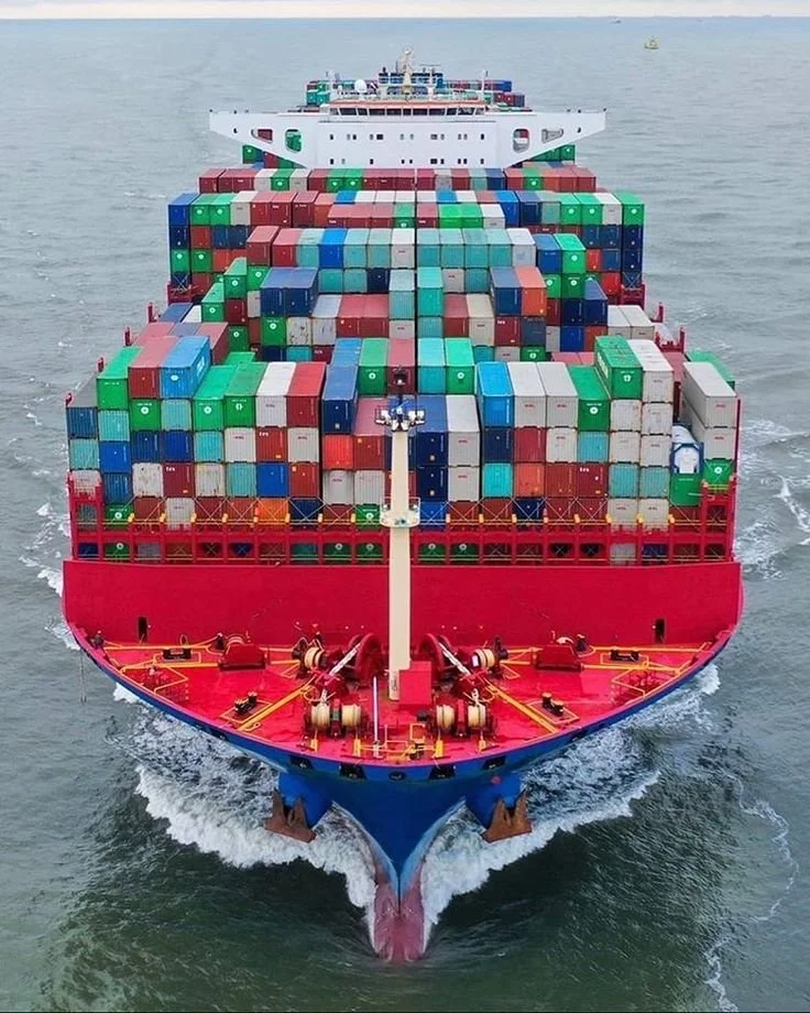 A large cargo ship sailing on the ocean, loaded with multicolored shipping containers.