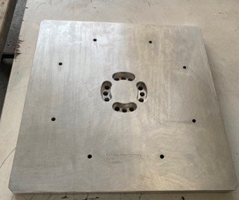 Metal plate with multiple drilled holes, including a central circular cutout and smaller holes around it.