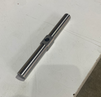 Metal cylindrical shaft with a hole in the middle, resting on a white surface.