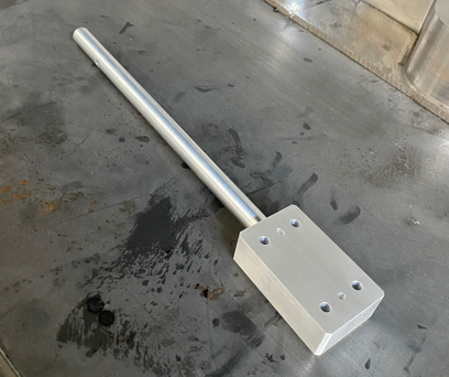 A metal chisel with a long handle and a rectangular blade on a dark, stained surface.