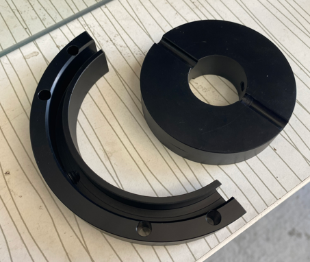 Two black circular metal components with holes, placed on a white wooden surface.