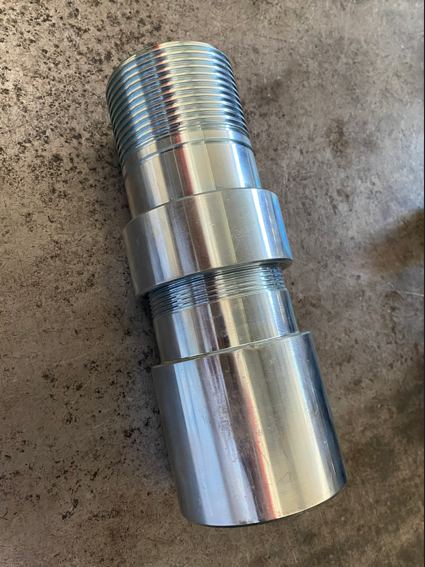 A metal, cylindrical object with threaded sections, lying on a concrete surface.