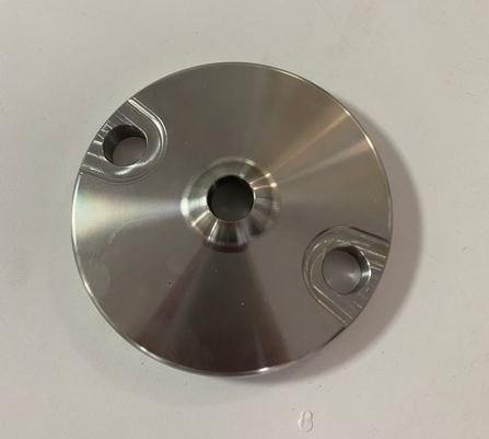 A shiny metal circular disc with three holes, lying on a white surface.