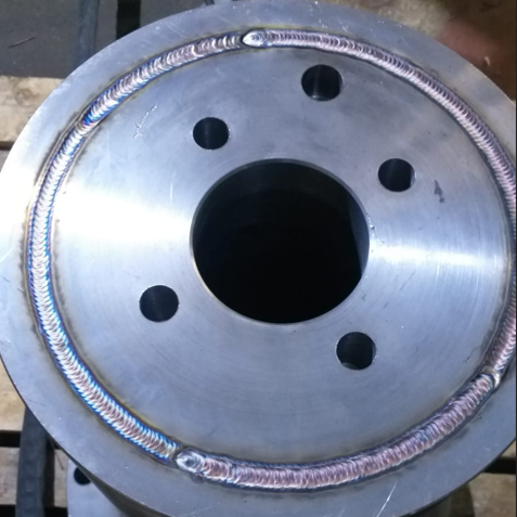 Close-up of a metal hub or flange with visible welding around the outer edge and five evenly spaced holes.