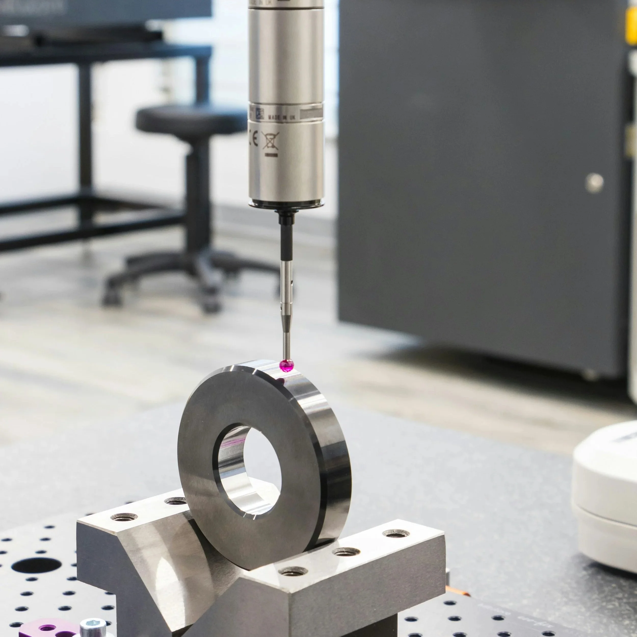 Close-up of a scientific instrument performing precision measurement on a metallic ring in a laboratory setting.