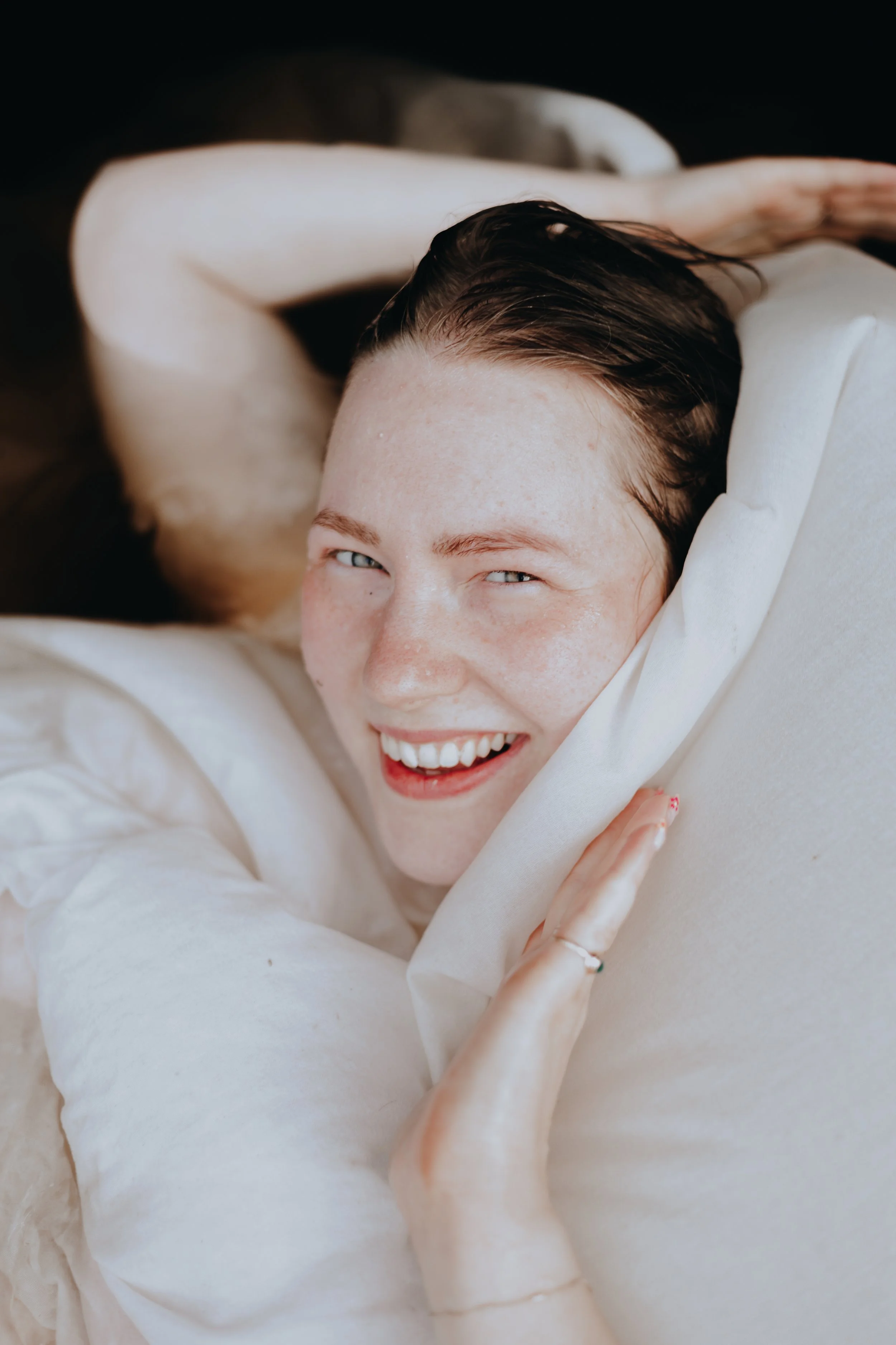 Iloinen nuori nainen, hänen hiuksensa ovat märät ja hän hymyilee leveästi näyttää olevan aurinkoinen ja iloinen tunnelma.