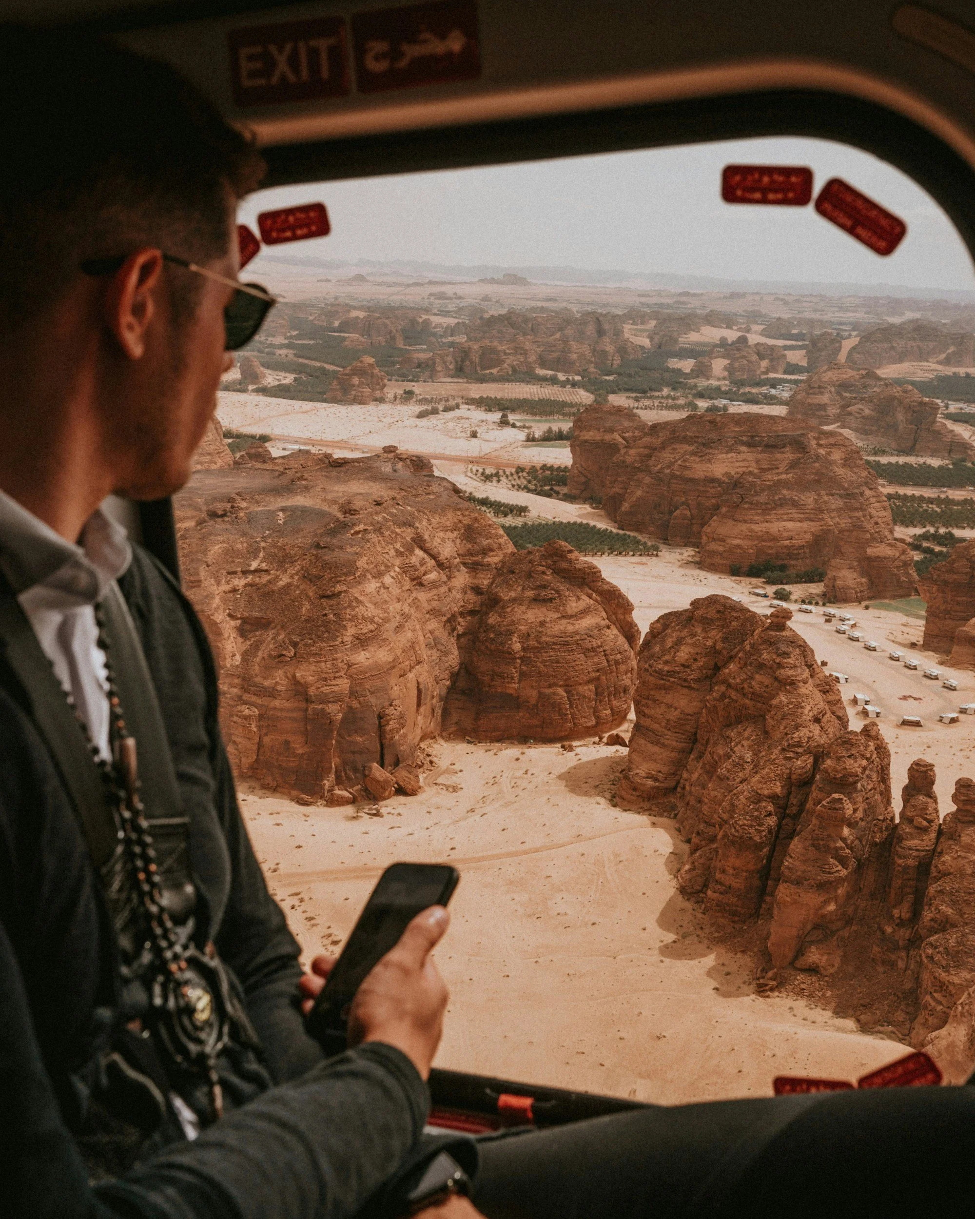 A man sitting inside a helicopter looking at a desert landscape with large rock formations.