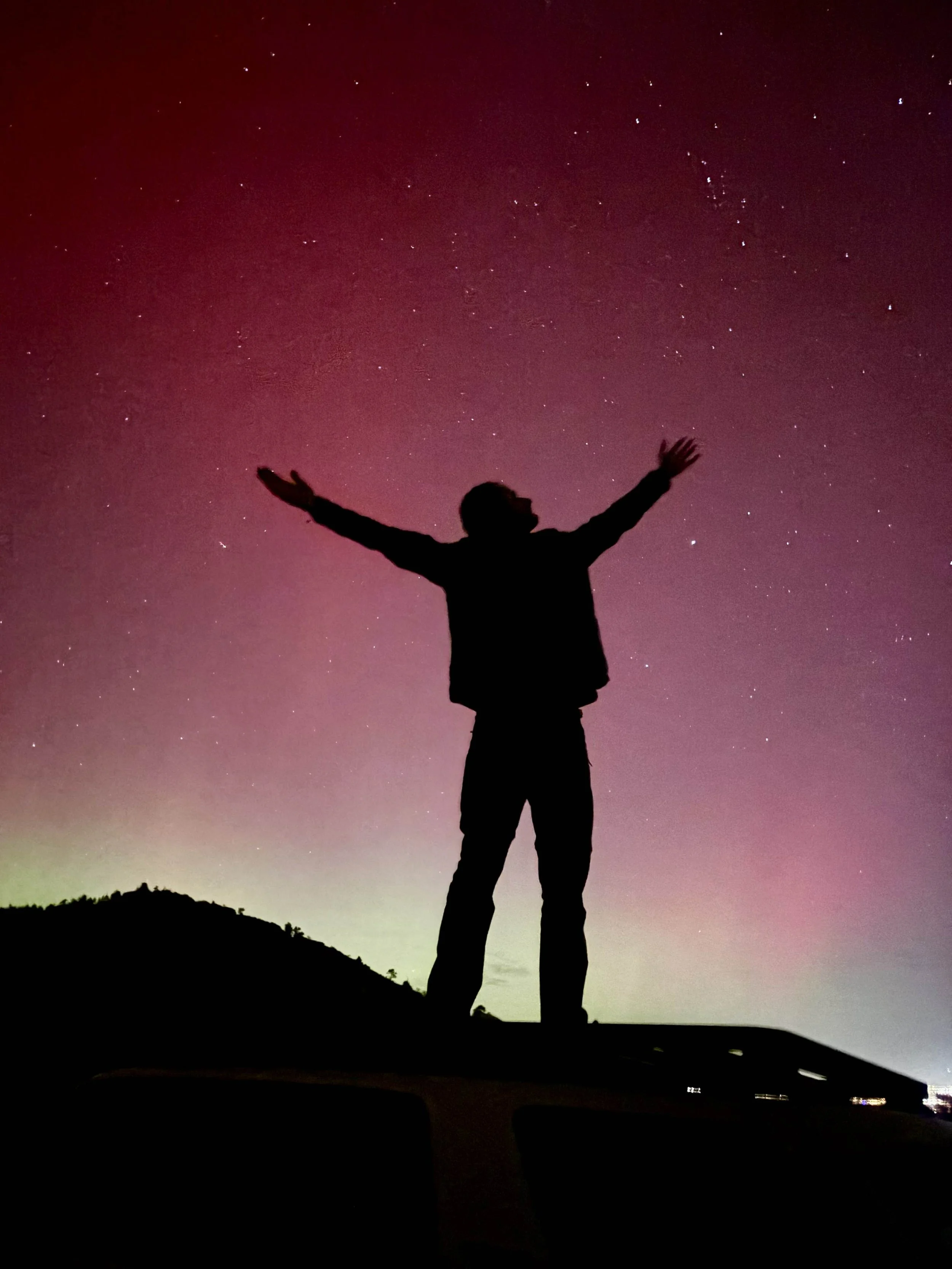 Silhouette of a person standing on a surface with arms outstretched under a colorful, starry night sky.