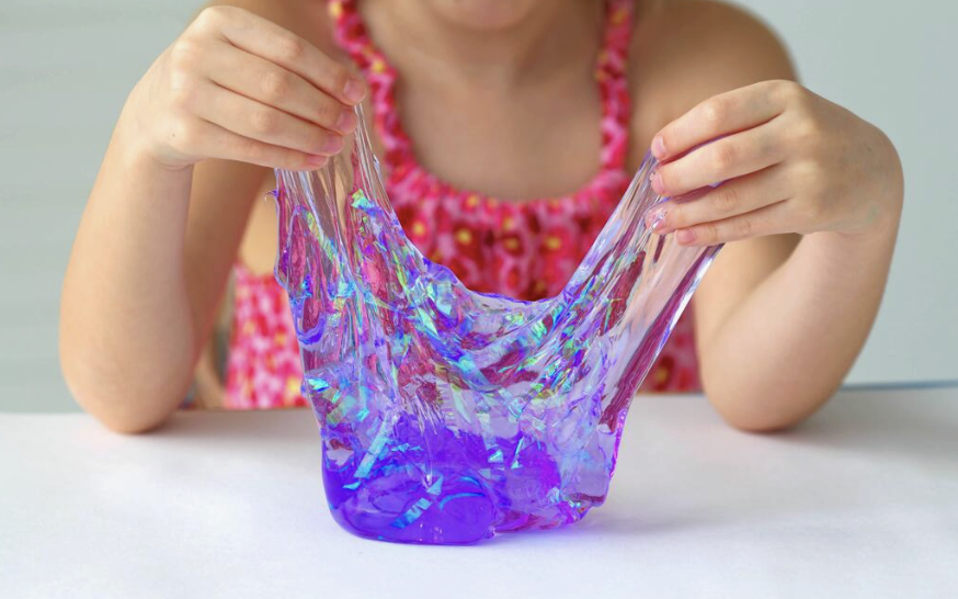Child playing with colorful, iridescent slime at a table.