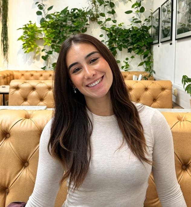 Digital illustration of a person wearing glasses and a black hijab, with a brown background.