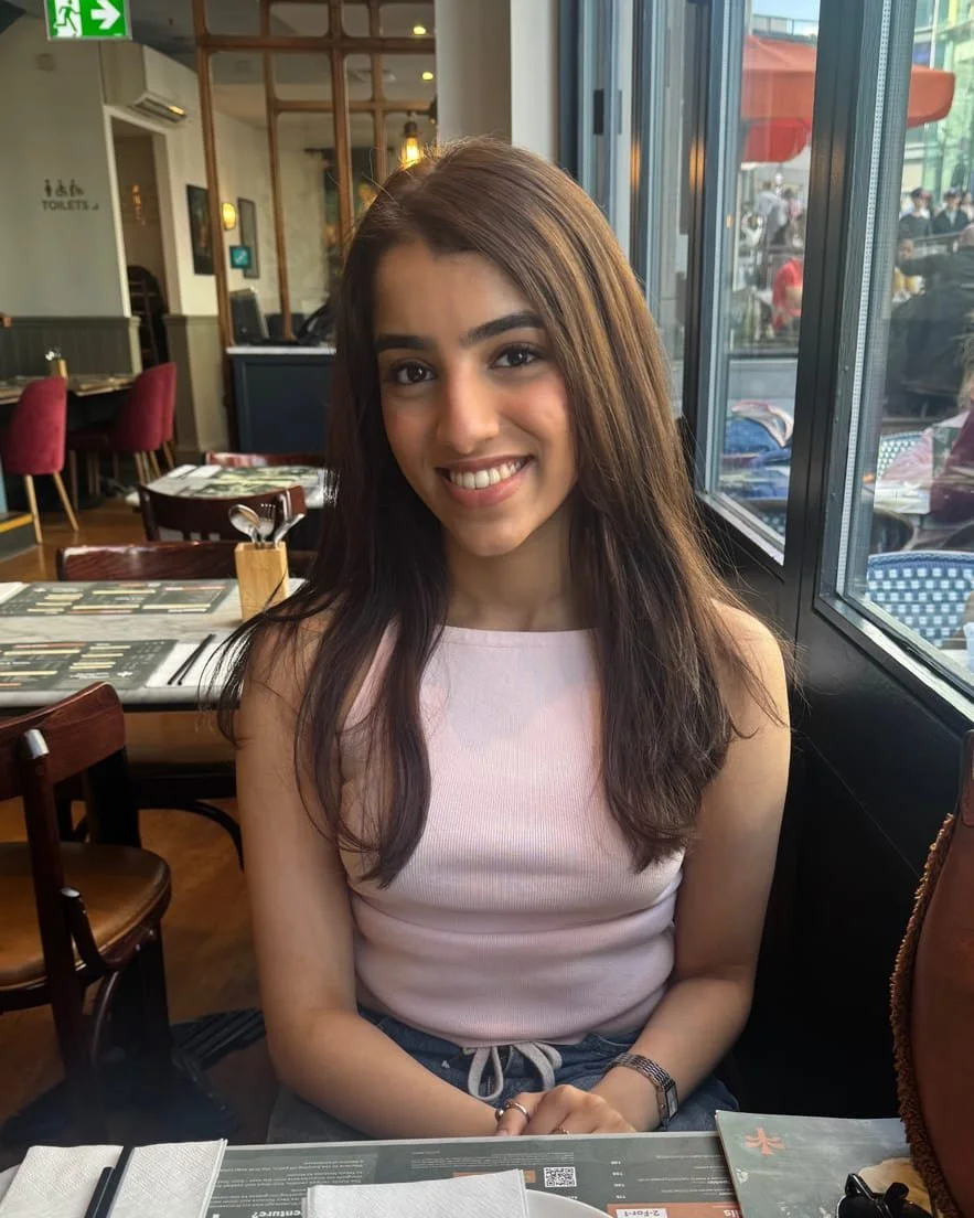 Illustration of a woman with long black hair, wearing a brown top and a light-colored collar, against a pale pink background.