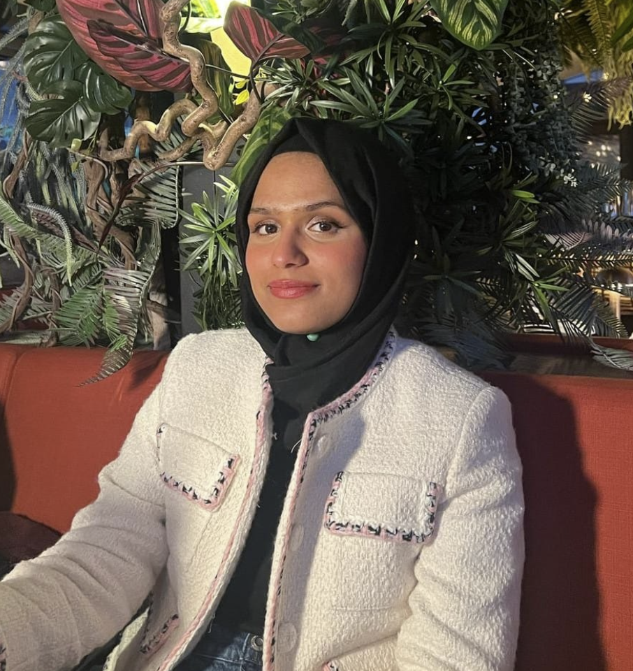 Minimalist digital illustration of a person wearing a black headscarf and red clothing, with a plain beige face and a solid blue background.