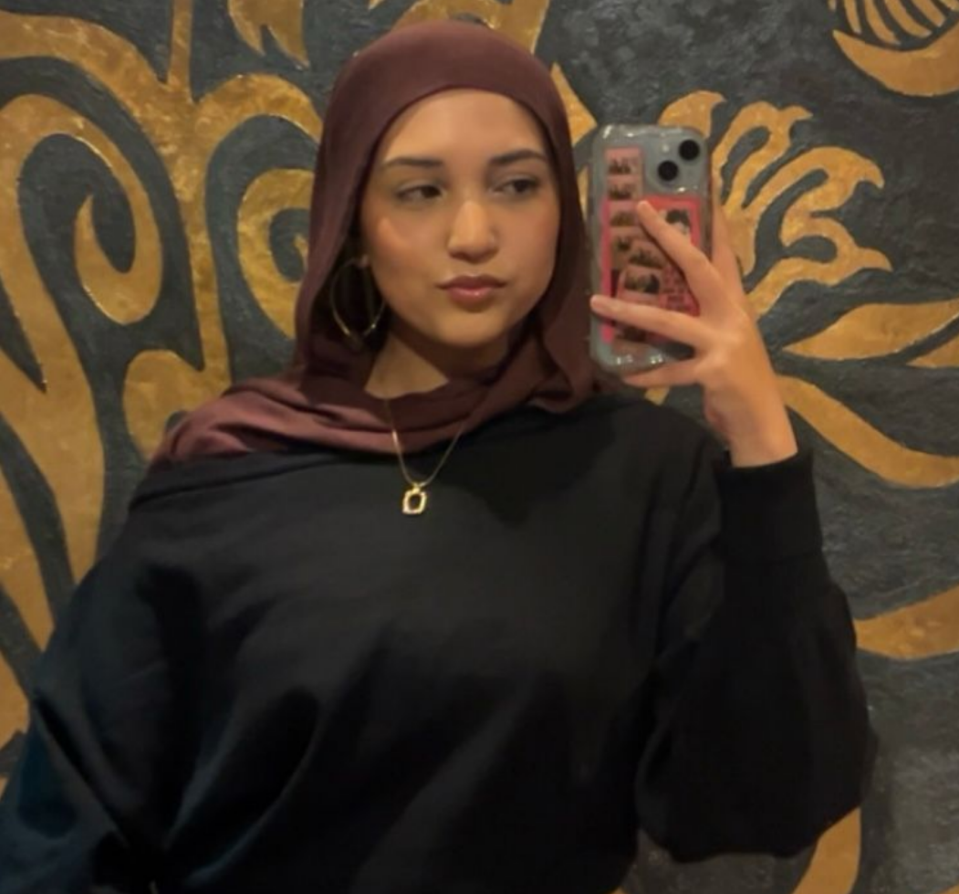 Digital illustration of a person wearing a black headscarf and gray shirt, with a yellow background, and no facial features.