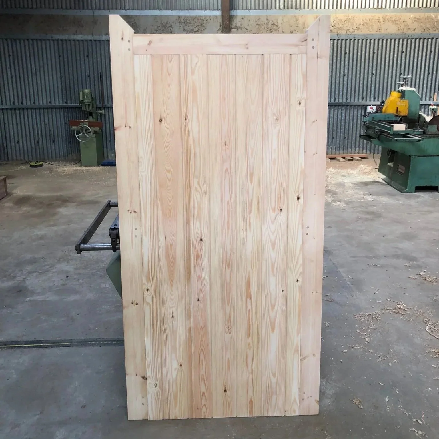 Wooden gate with a rounded top, set into a brick wall, surrounded by green foliage and trees, with sunlight filtering through.