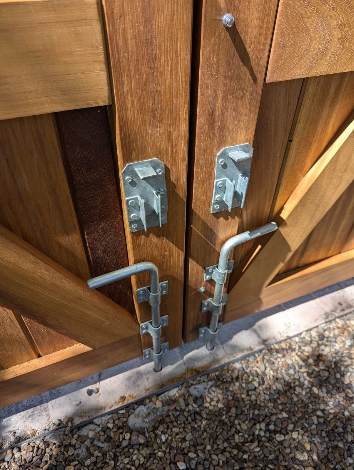 Wooden gate secured with metal latch and bolt, with metal hinges, on a gravel ground.