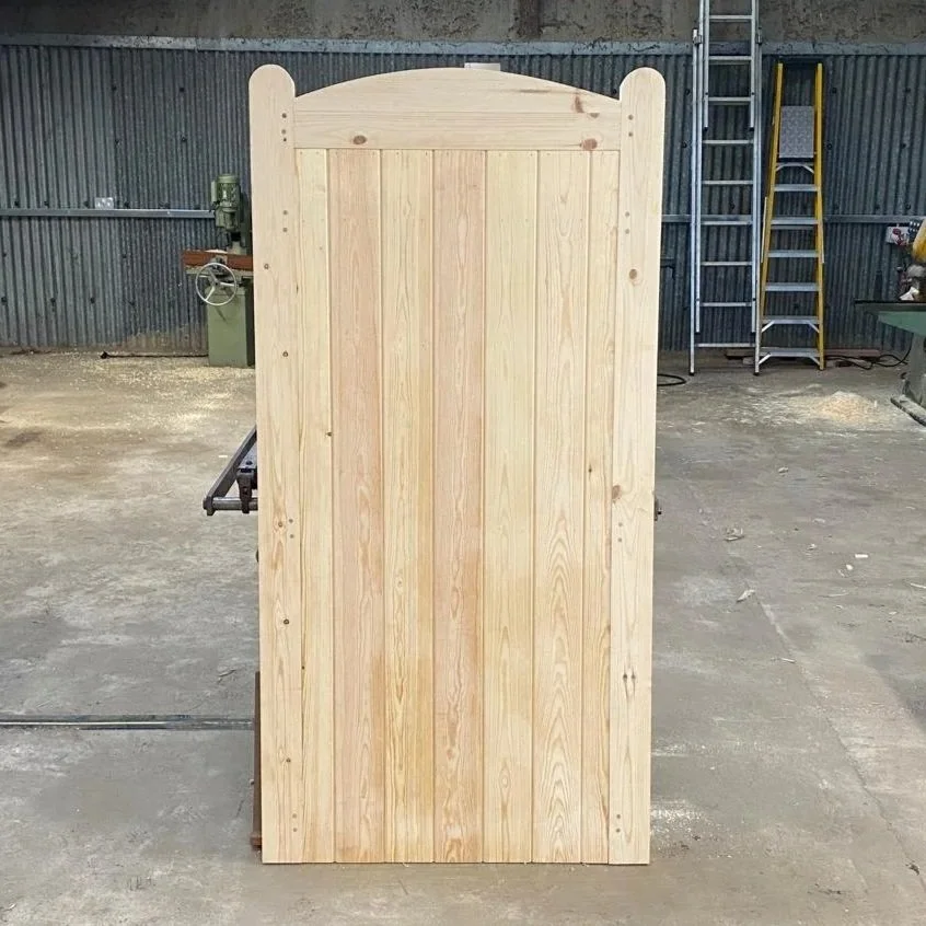 Wooden gate with a rounded top, set into a brick wall, surrounded by green foliage and trees, with sunlight filtering through.