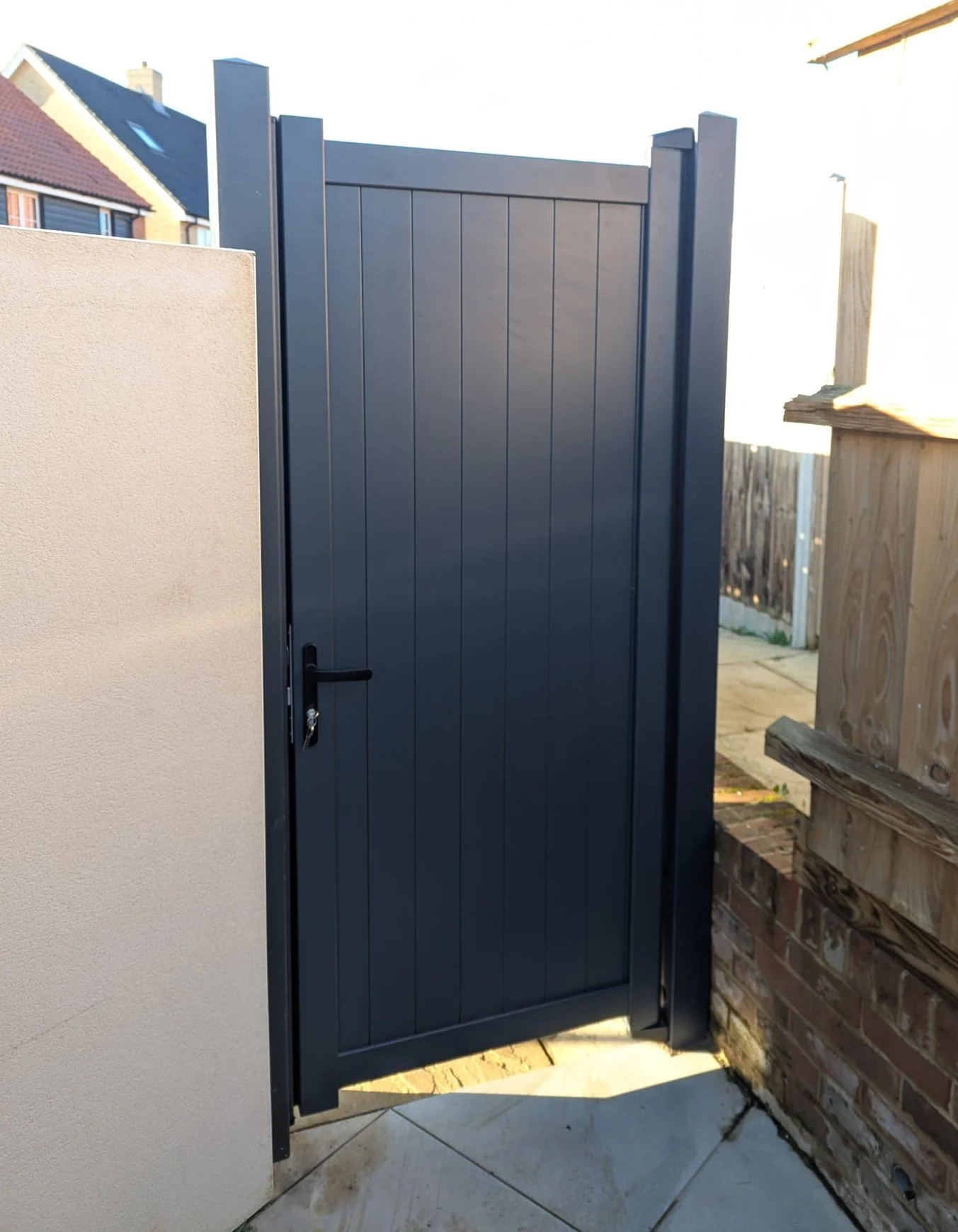 Black privacy gate with vertical panels, secured with a lock, part of an outdoor backyard area.