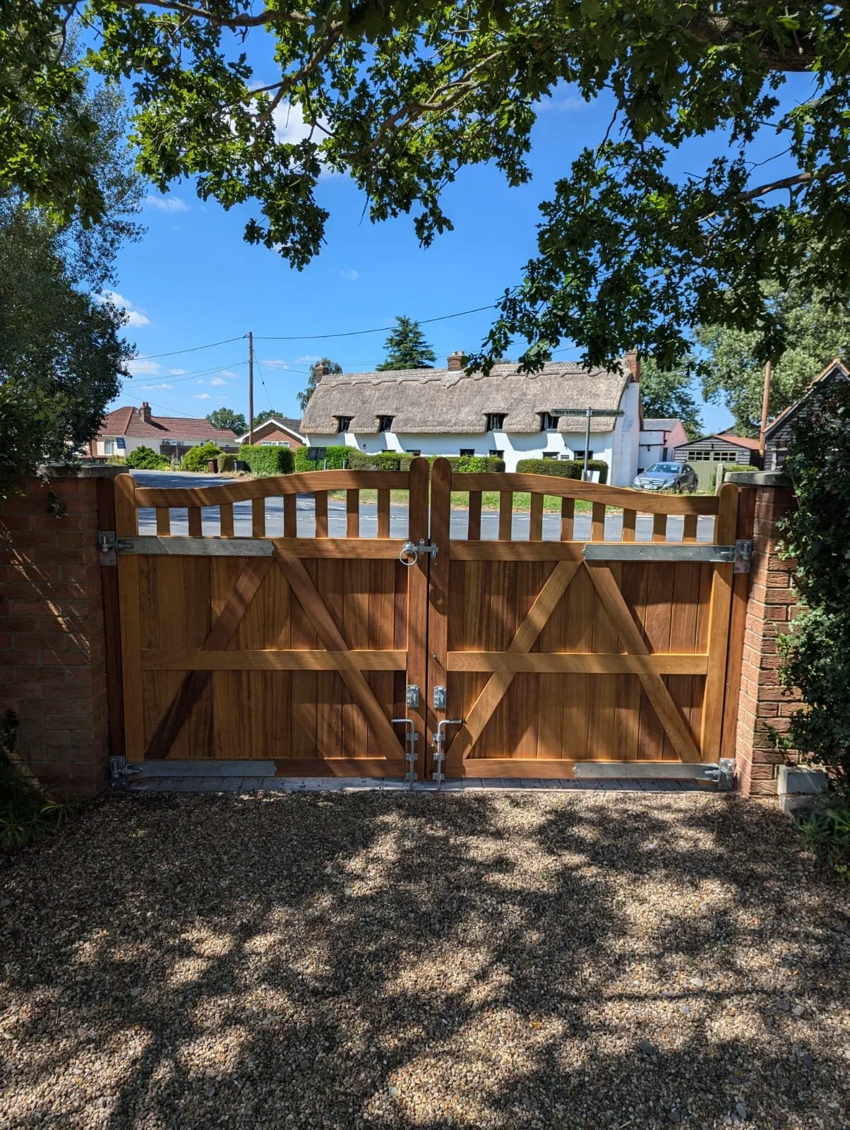 View of a wooden gate and brick wall with a residential neighborhood in the background, under a partly cloudy sky with trees.
