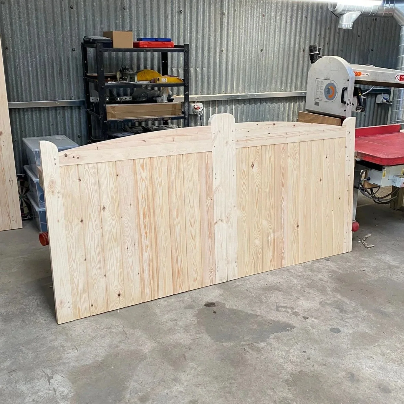 Wooden gate with brick pillars in front of a house with a red-tile roof and dormer windows, surrounded by greenery and trees.