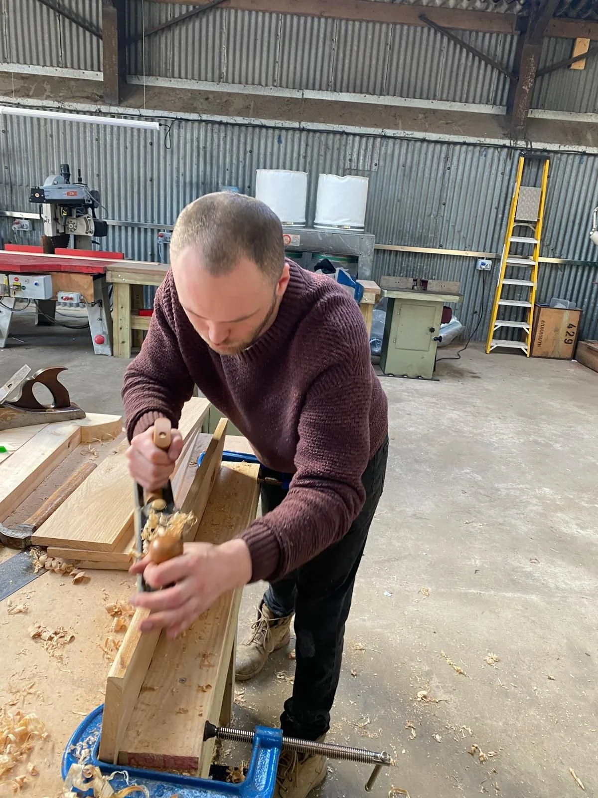 Man working with a hand plane on a piece of wood in a woodworking workshop.