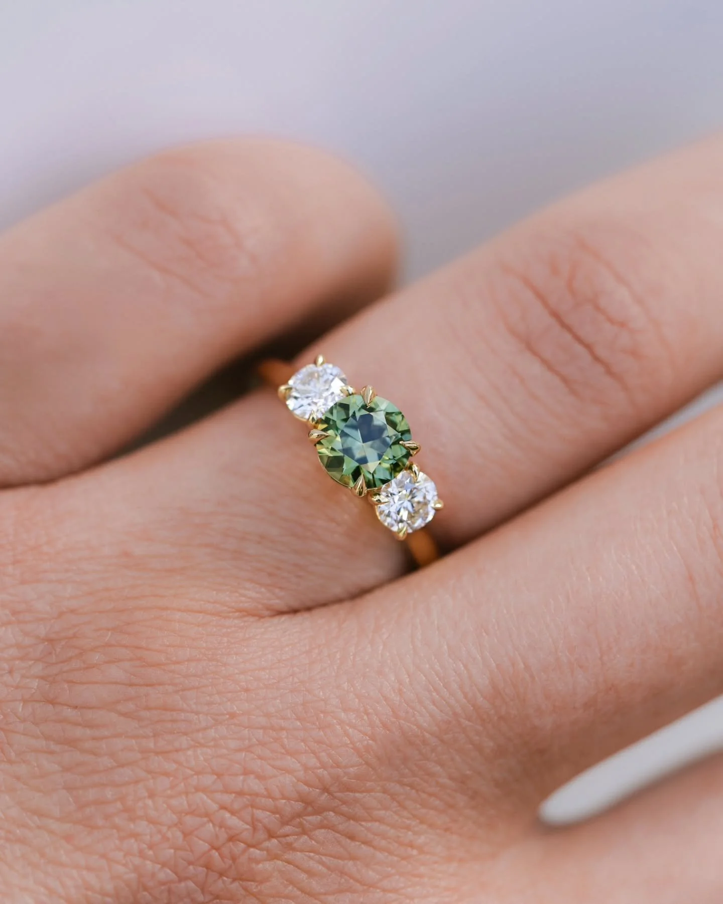 This trilogy ring holds a soft green sapphire at its centre, natural and unheated, mined and cut in the Queensland gemfields by the same a one-man operation. It&rsquo;s flanked by two sparkling natural round diamonds. A trilogy ring with a story as b