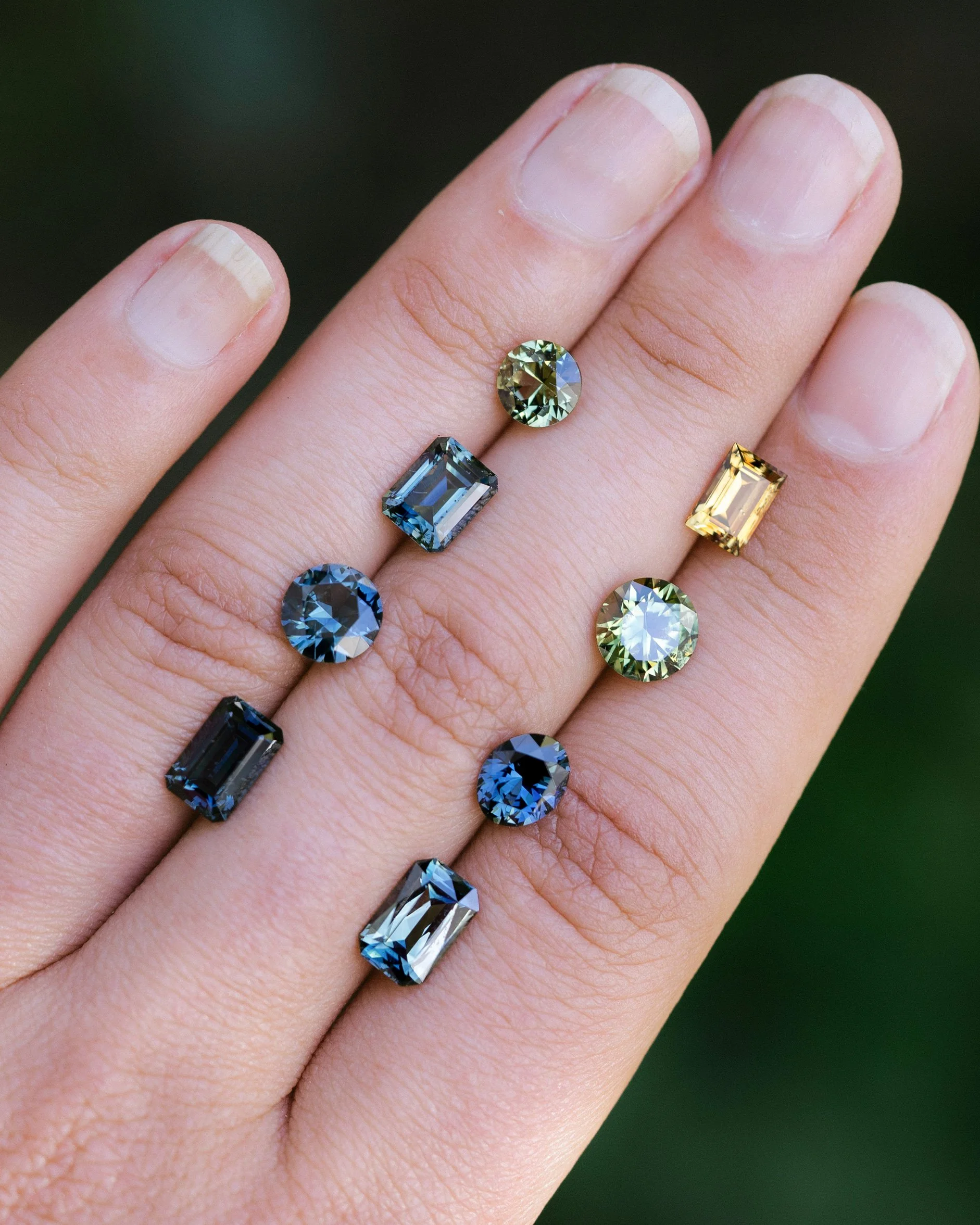 A hand with multiple colorful gemstones of various shapes and sizes resting on the fingers.