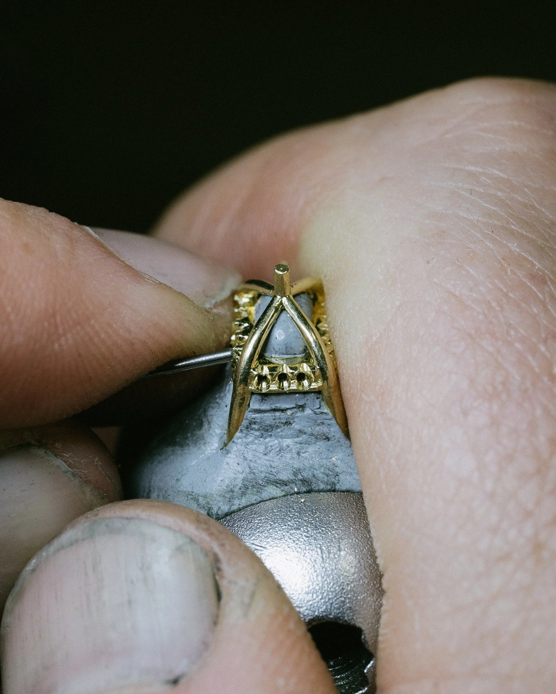 Close-up of a gold ring with white diamonds, placed on a grey shellac, used for stone setting.