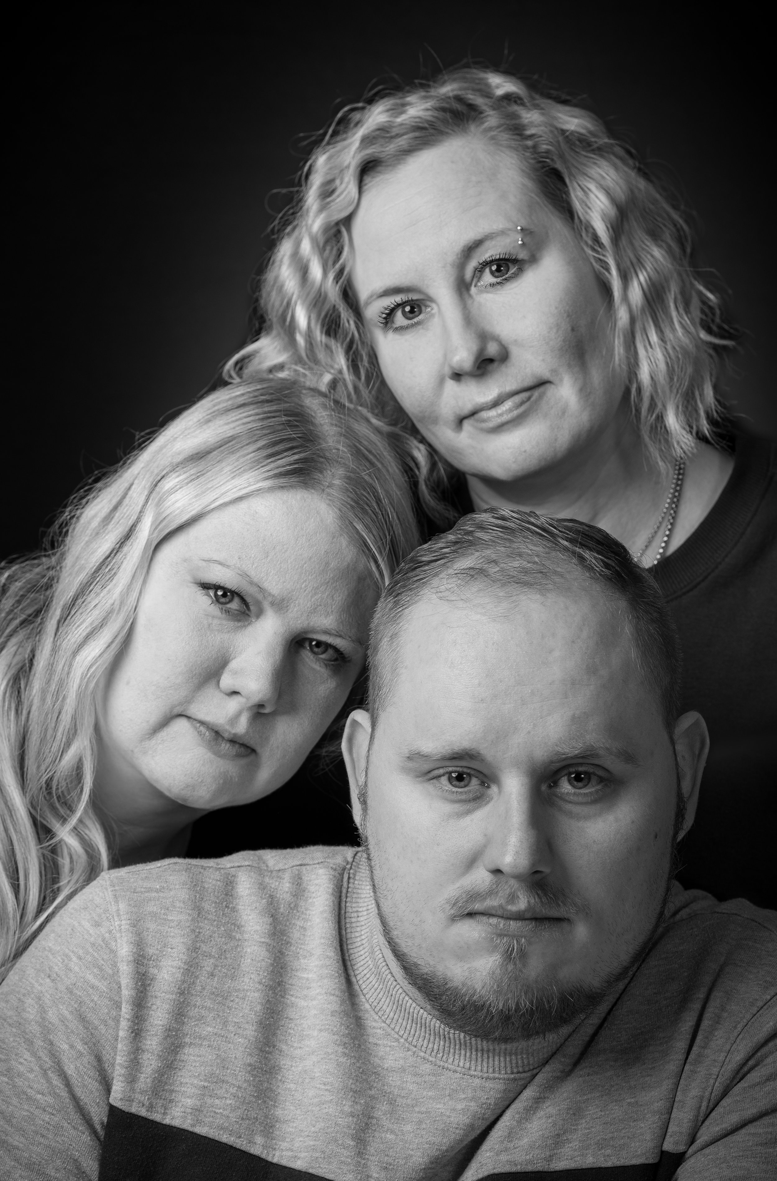 Mustavalkoinen valokuva kolmihenkisestä perheestä, kolme ihmistä, kaksi naista ja yksi mies, kuva otettu studiovalossa, vakava ilme, mustavalkoinen