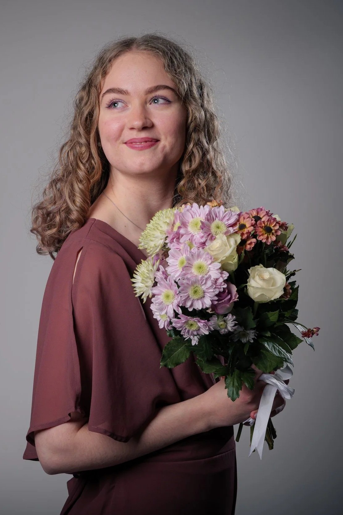 Nuori nainen pitelee kukkakimppua, katsoo sivuun, taustalla harmaa.