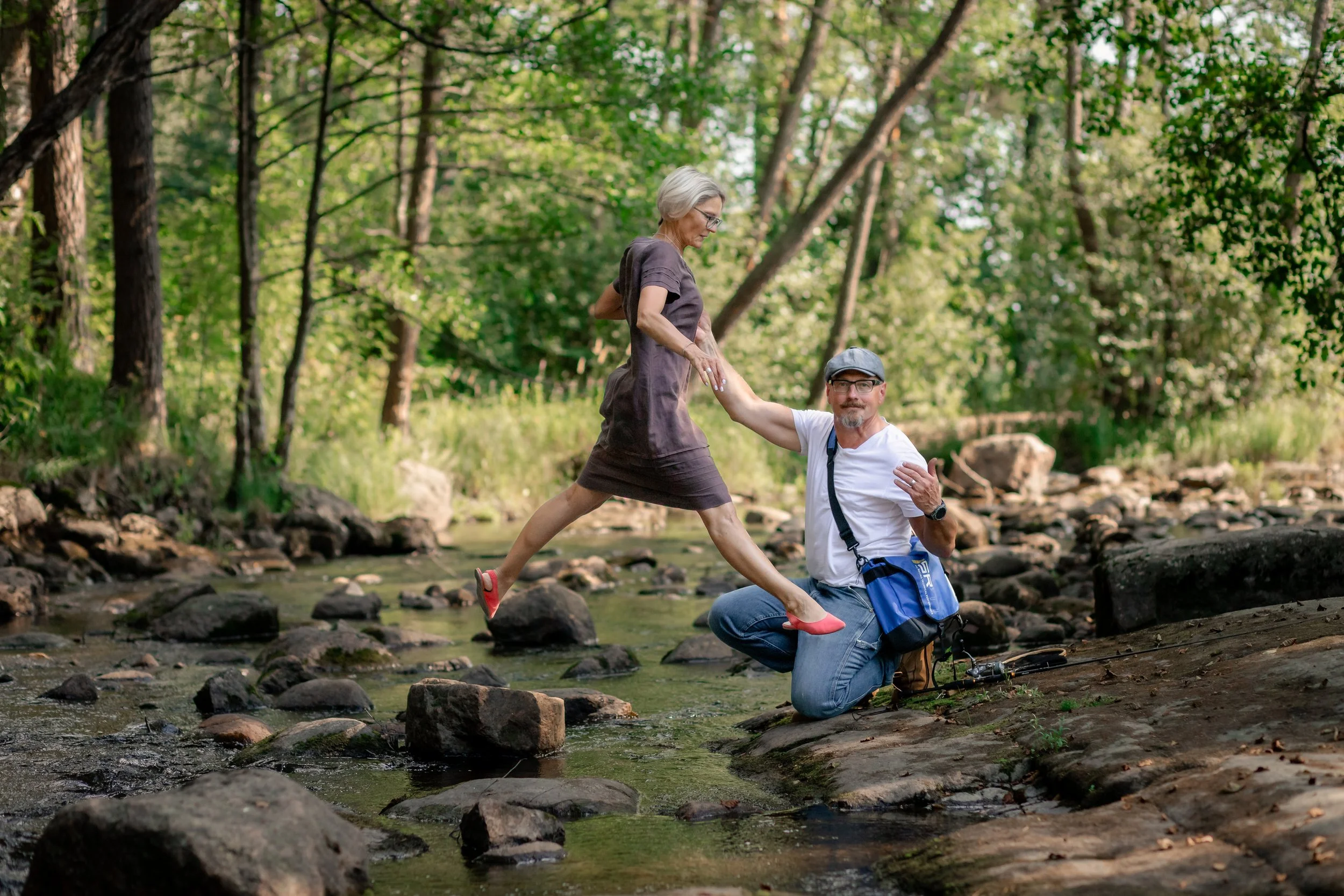 Mies ja nainen ulkona luonnossa, mies polvistuneena ja nainen kävelee.