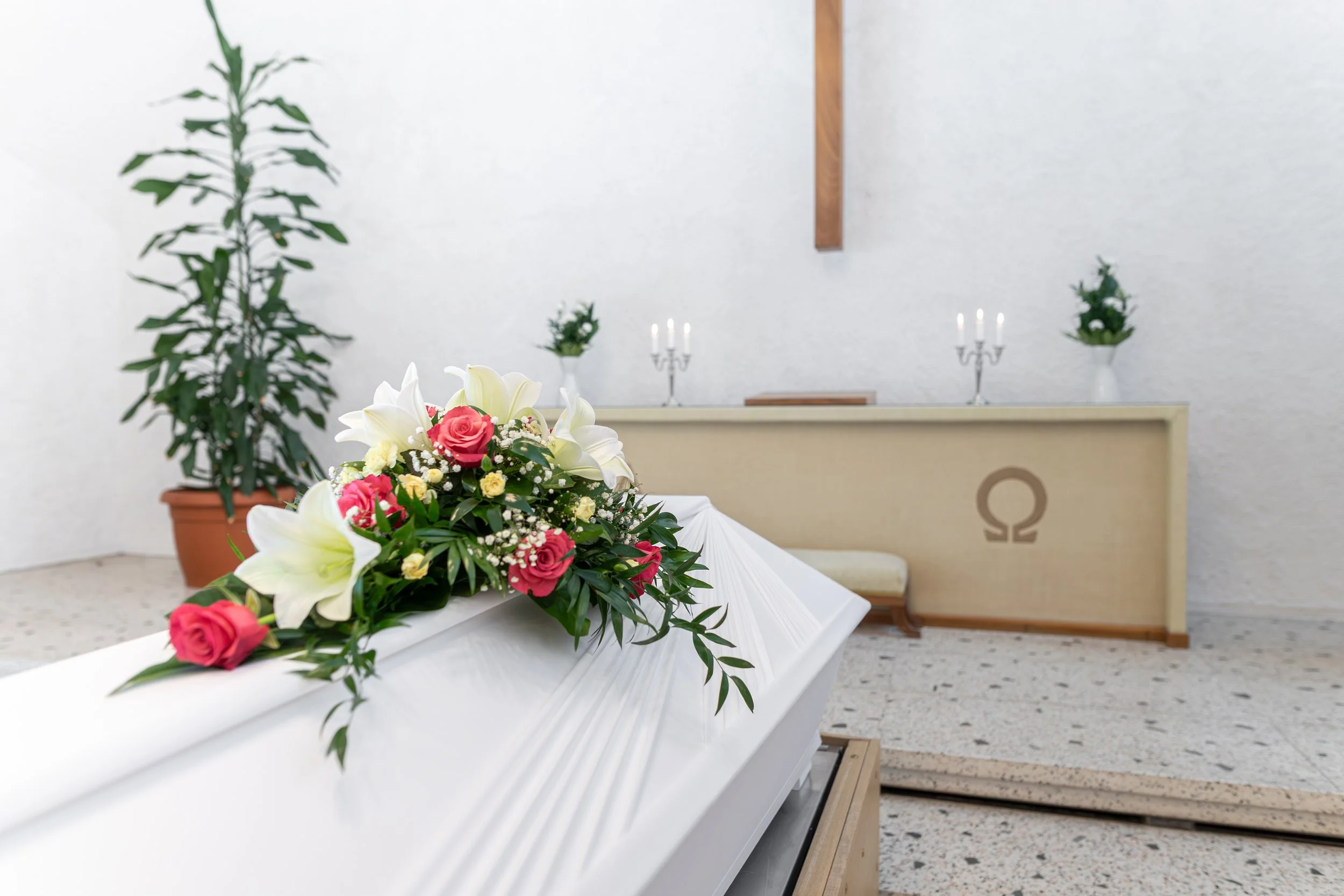 Häälävaatteinen valkoinen arkku kukkakoristeineen edessä kirkossa alttarilla.