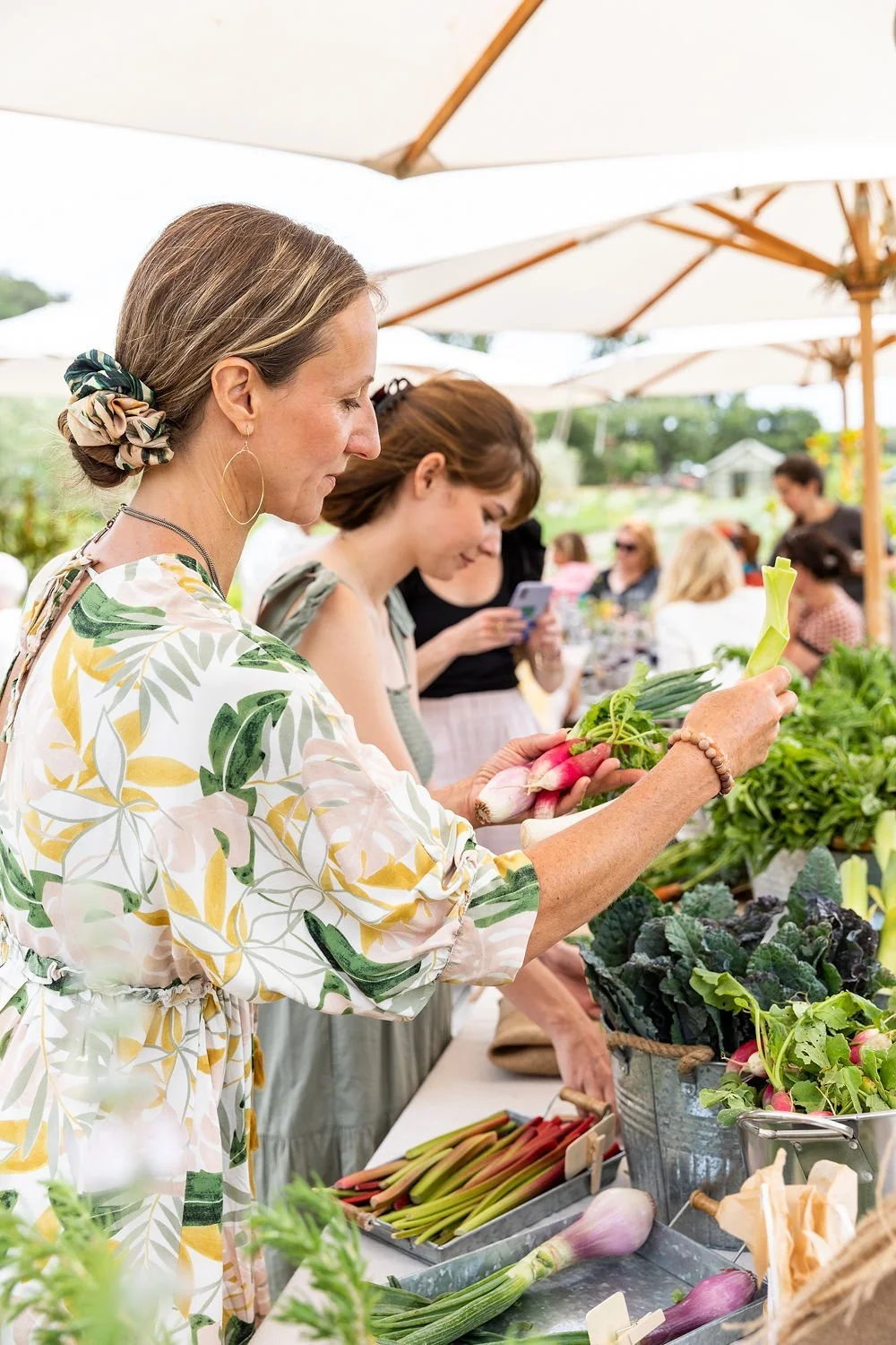 Women shopping for fresh vegetables at an outdoor farmers market.