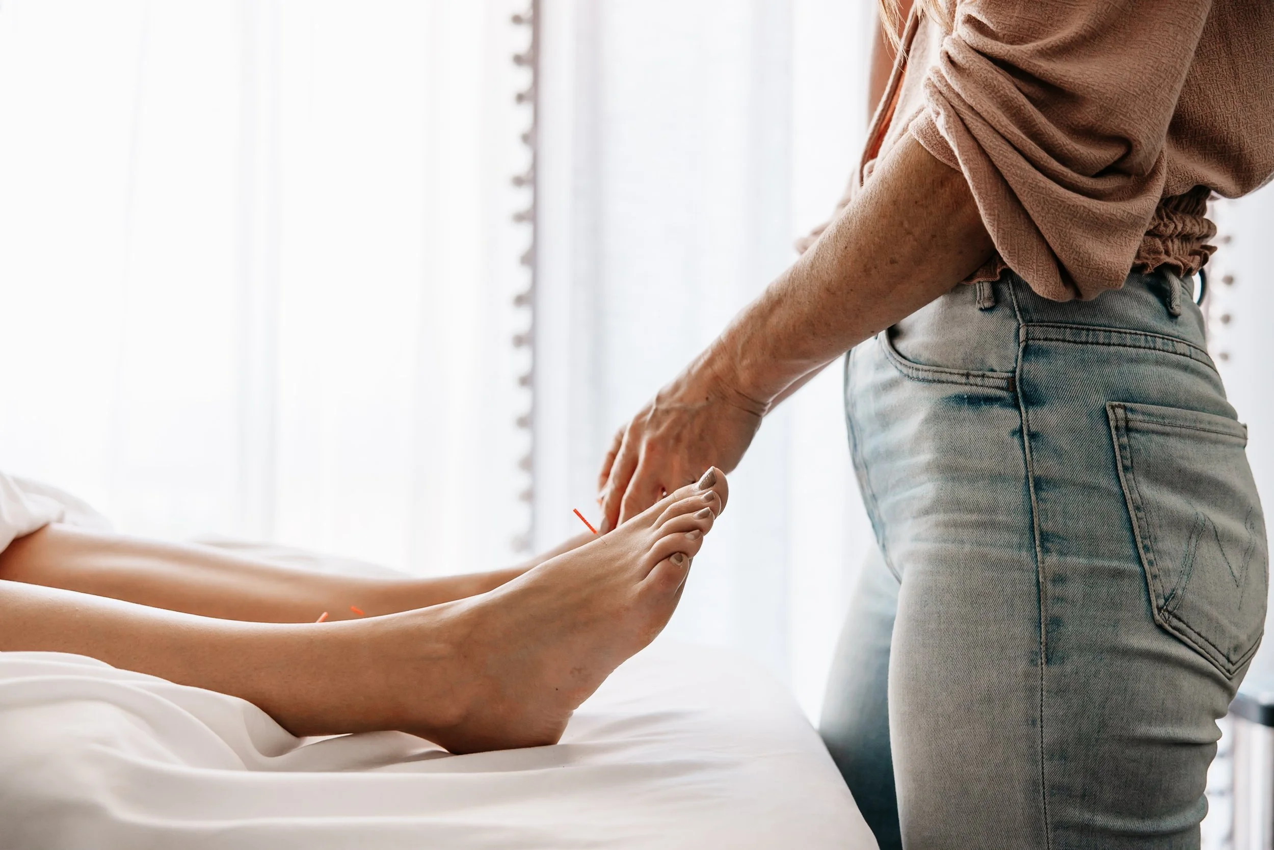 A person receiving foot acupuncture treatment while lying in bed, with another person standing beside them.