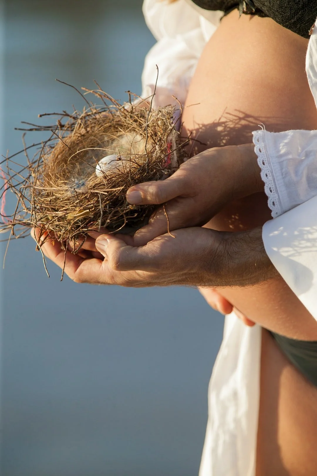 A person holding a bird's nest with an egg inside, close to a body of water.