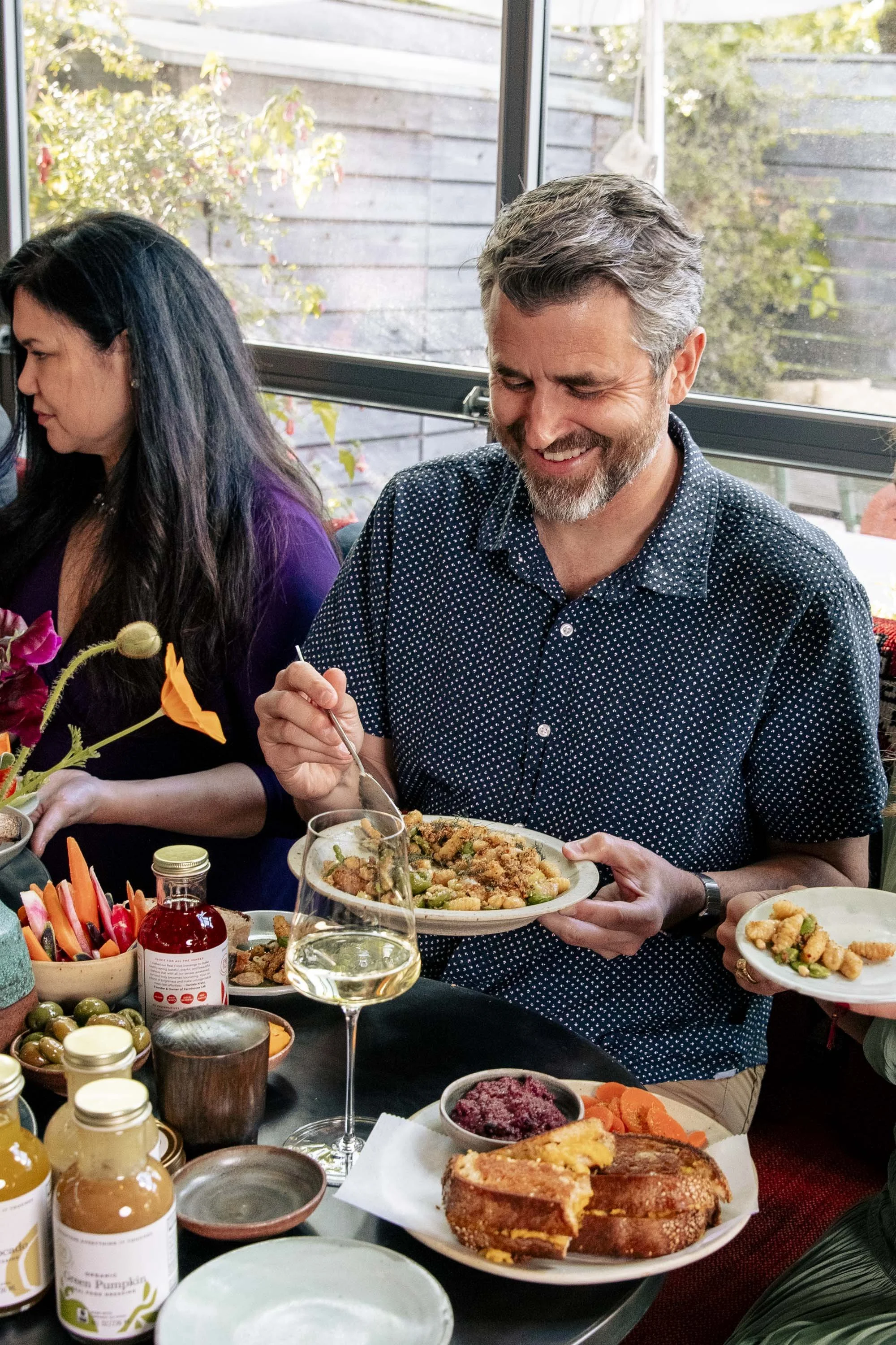 Man smiling and serving food at a family gathering dinner with various dishes and condiments on the table.