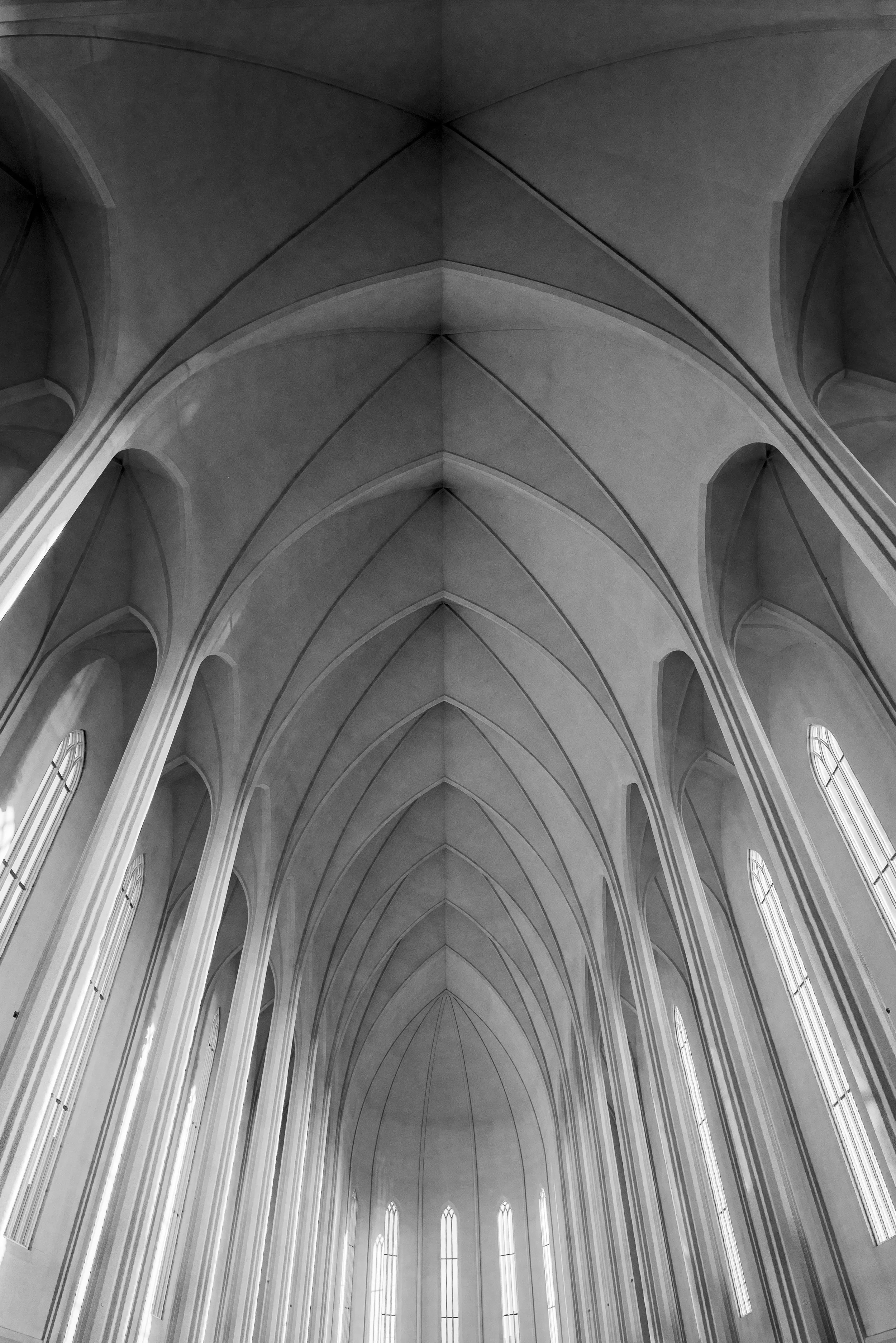 Black and white photograph of a cathedral interior ceiling with pointed arches and tall narrow windows.