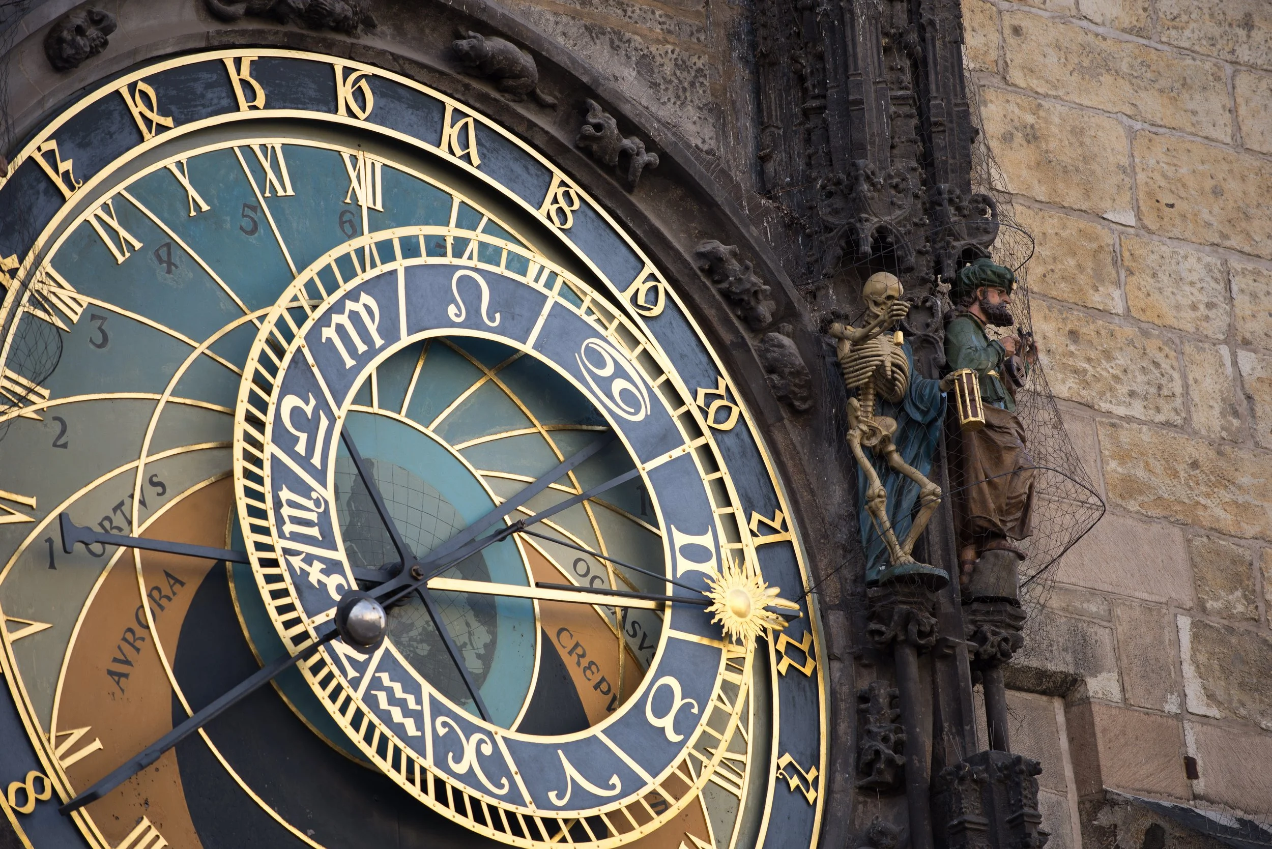 Close-up of an ornate astronomical clock on a historic stone building, with detailed sculptures and zodiac symbols.