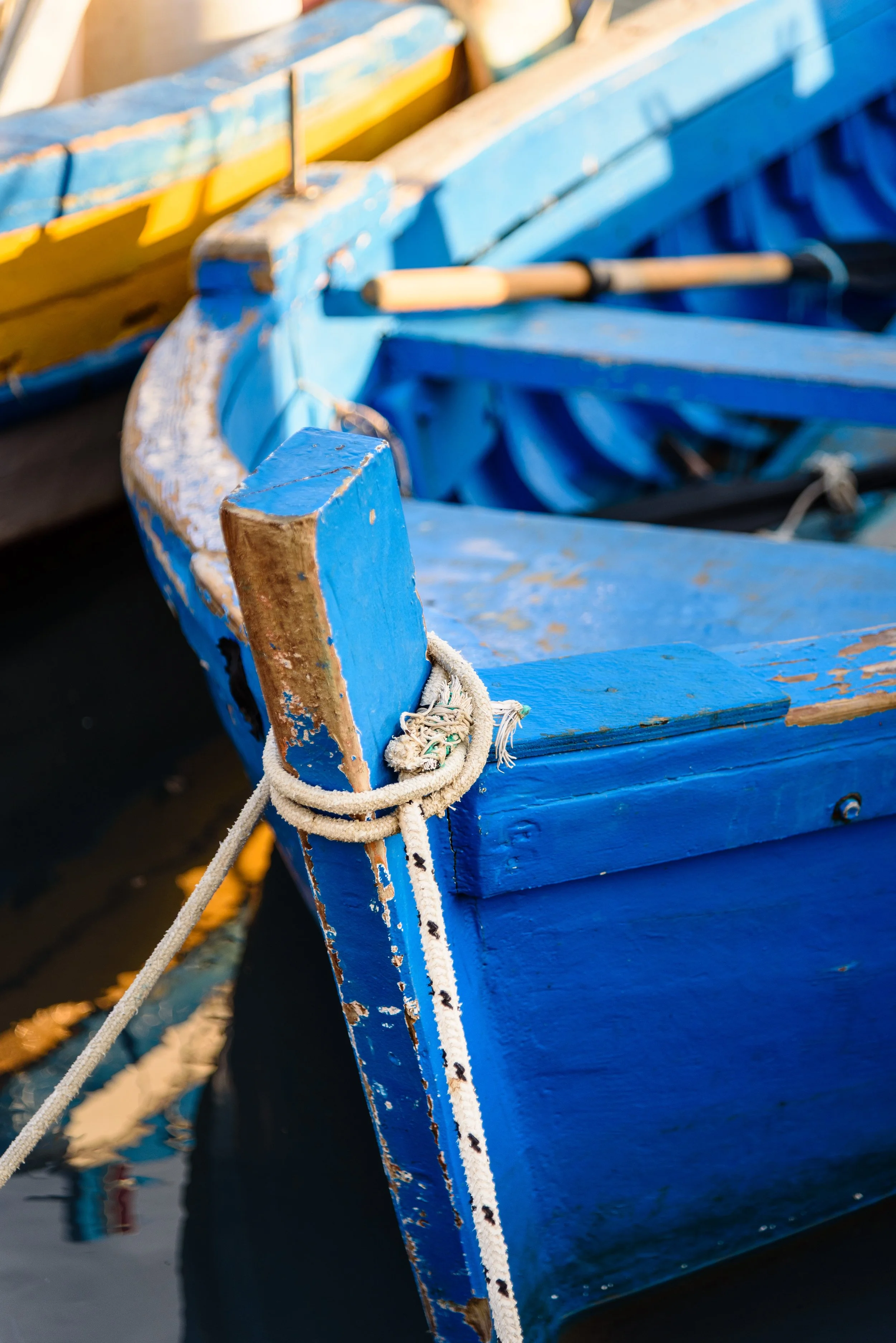 Close-up of a worn blue wooden boat tied with a rope to a dock.