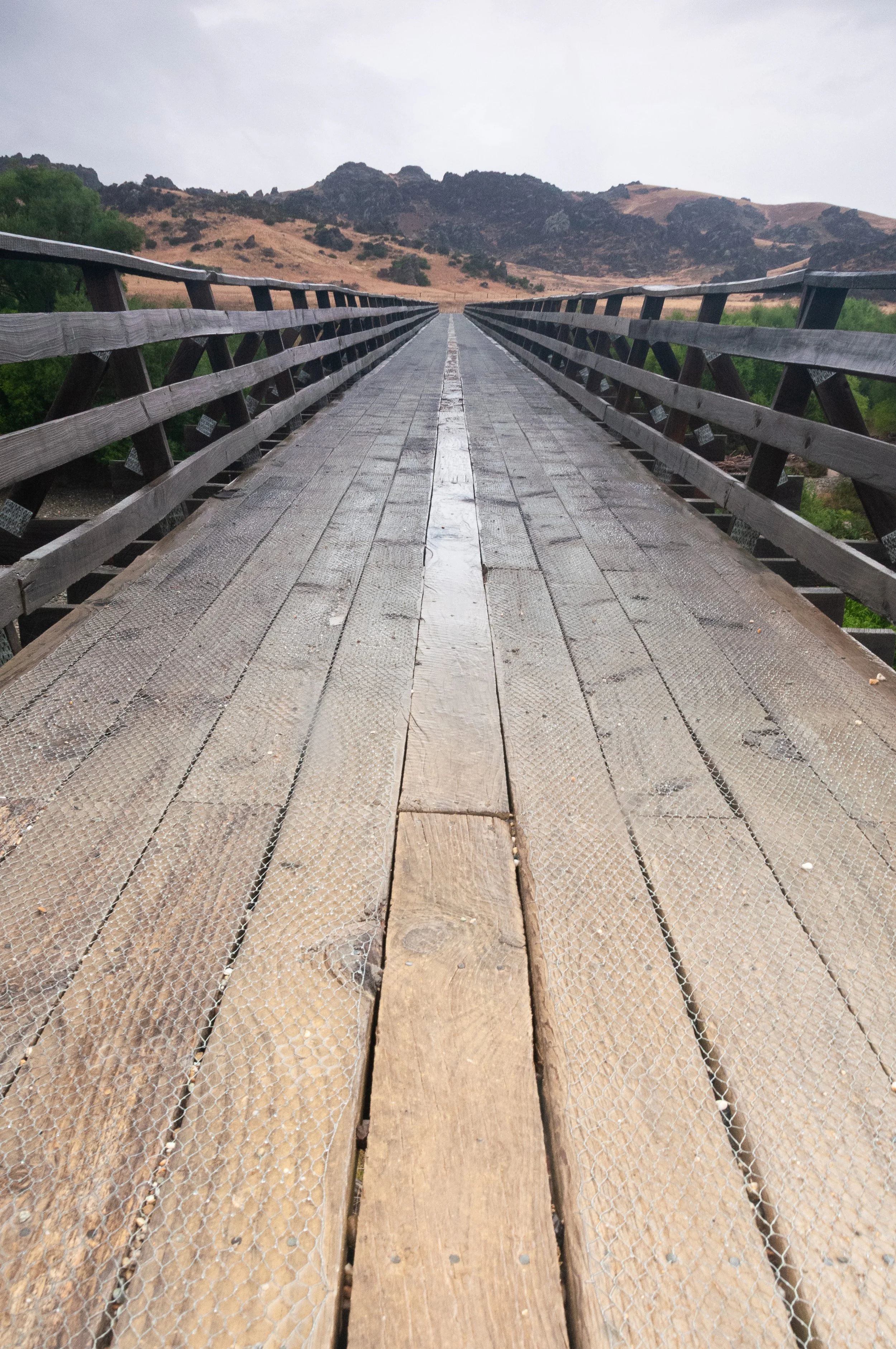 Wooden bridge with metal railings extending towards mountainous landscape in the distance.