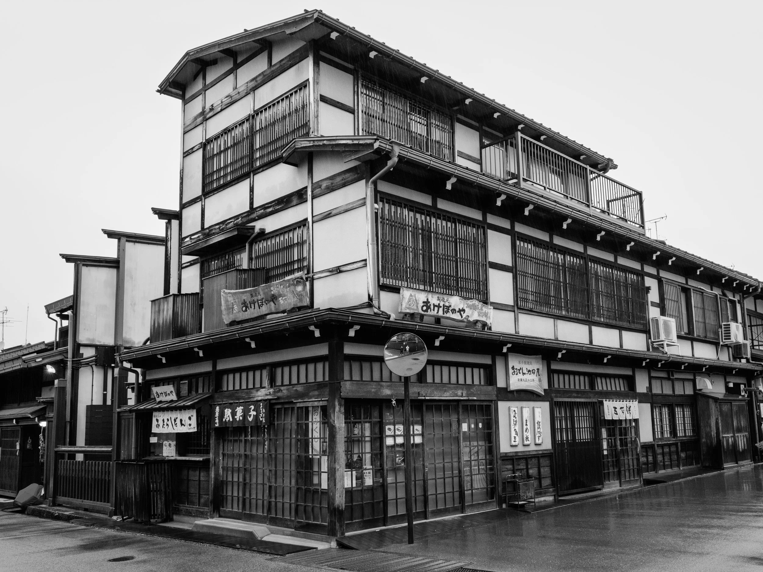 Traditional Japanese building with multiple stories, wooden frames, shoji-style sliding windows, and signs written in Japanese characters, located on an empty street.