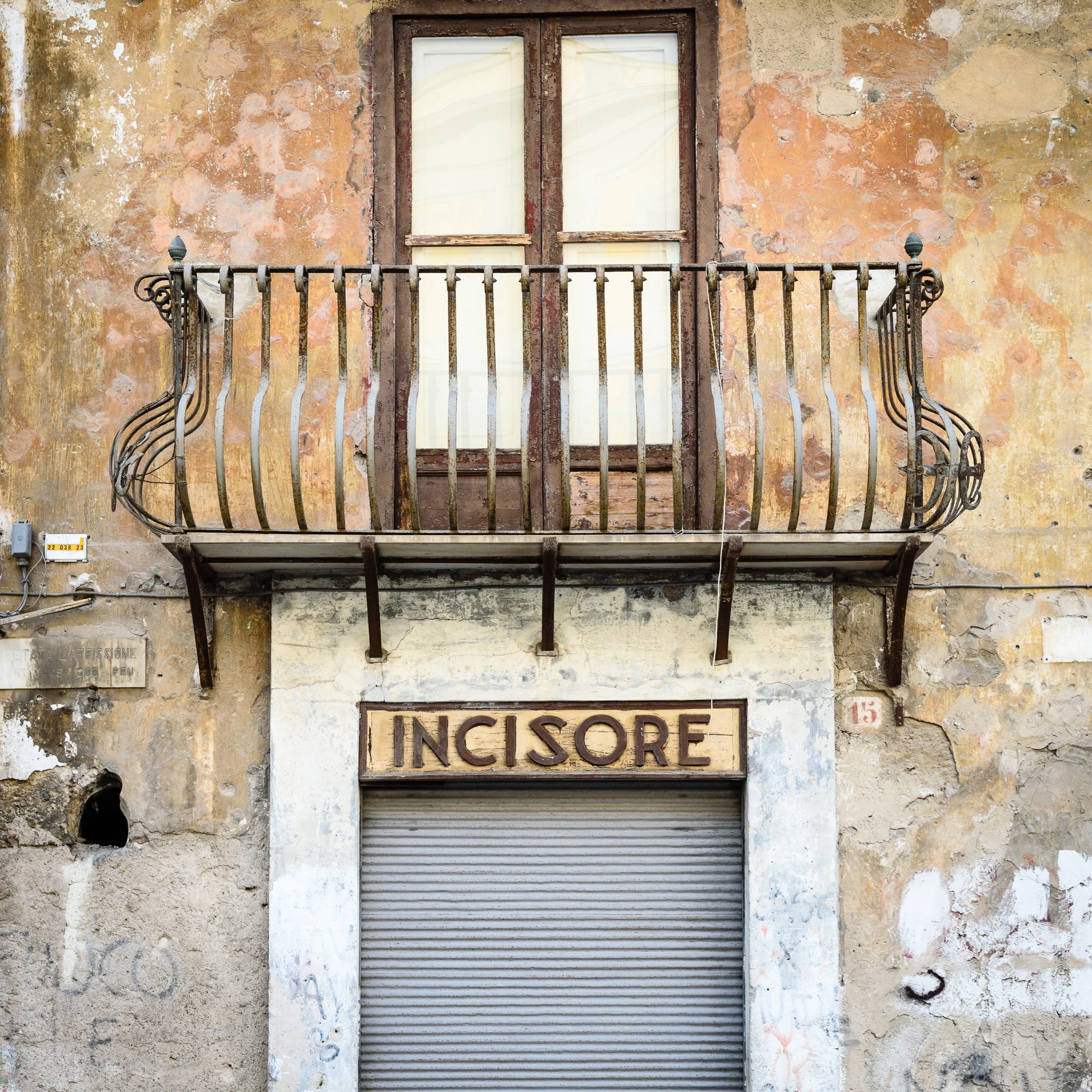 An old, weathered building with a small wrought iron balcony above a shuttered storefront, with the sign 'INCISORE' in worn letters.