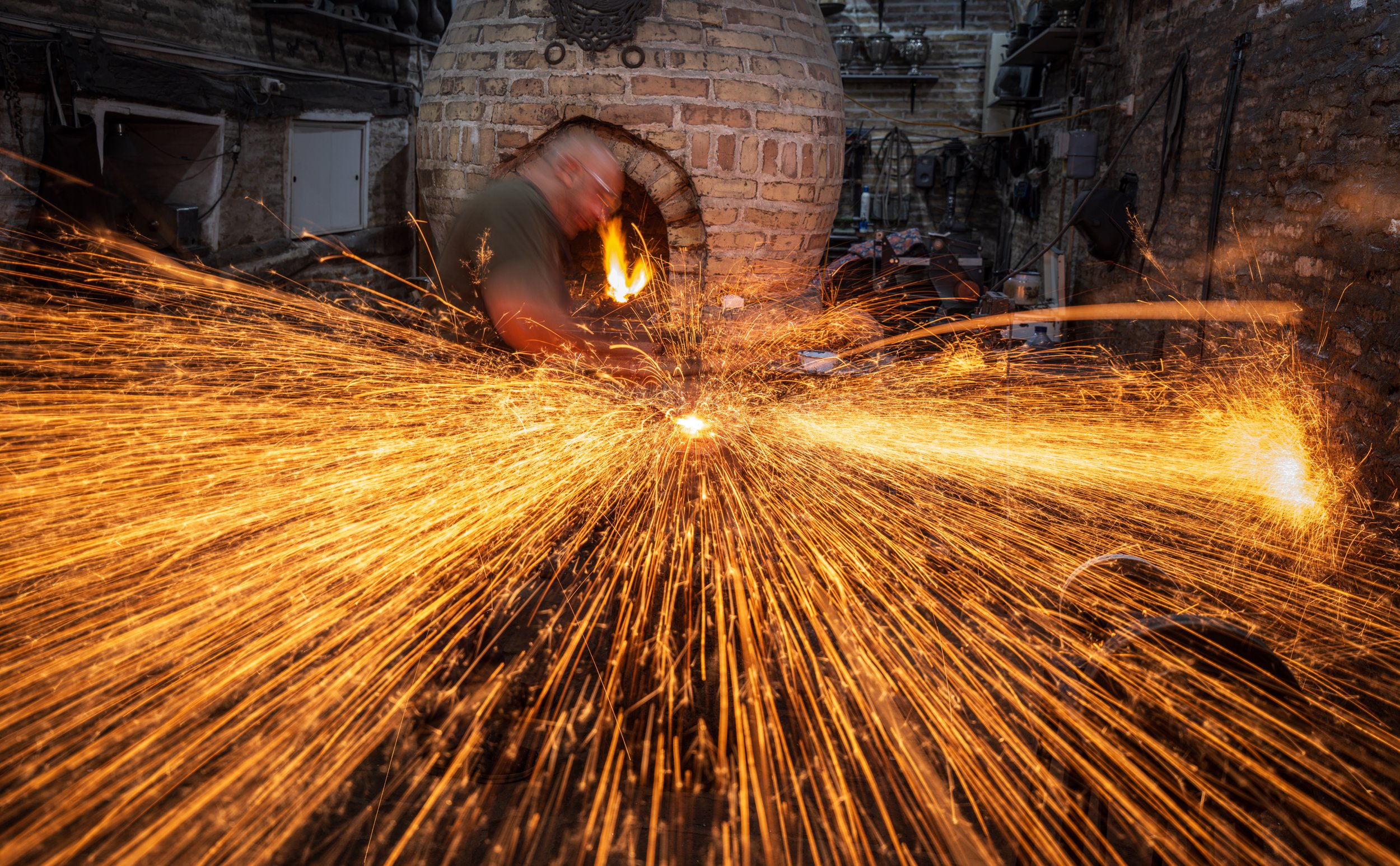 A person welding with sparks flying in a brick workshop or forge.