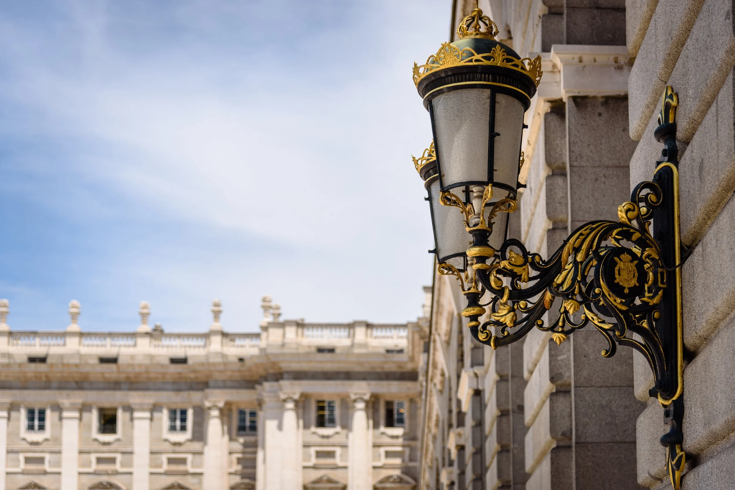 Ornate black and gold wrought iron outdoor lamp mounted on a brick building.