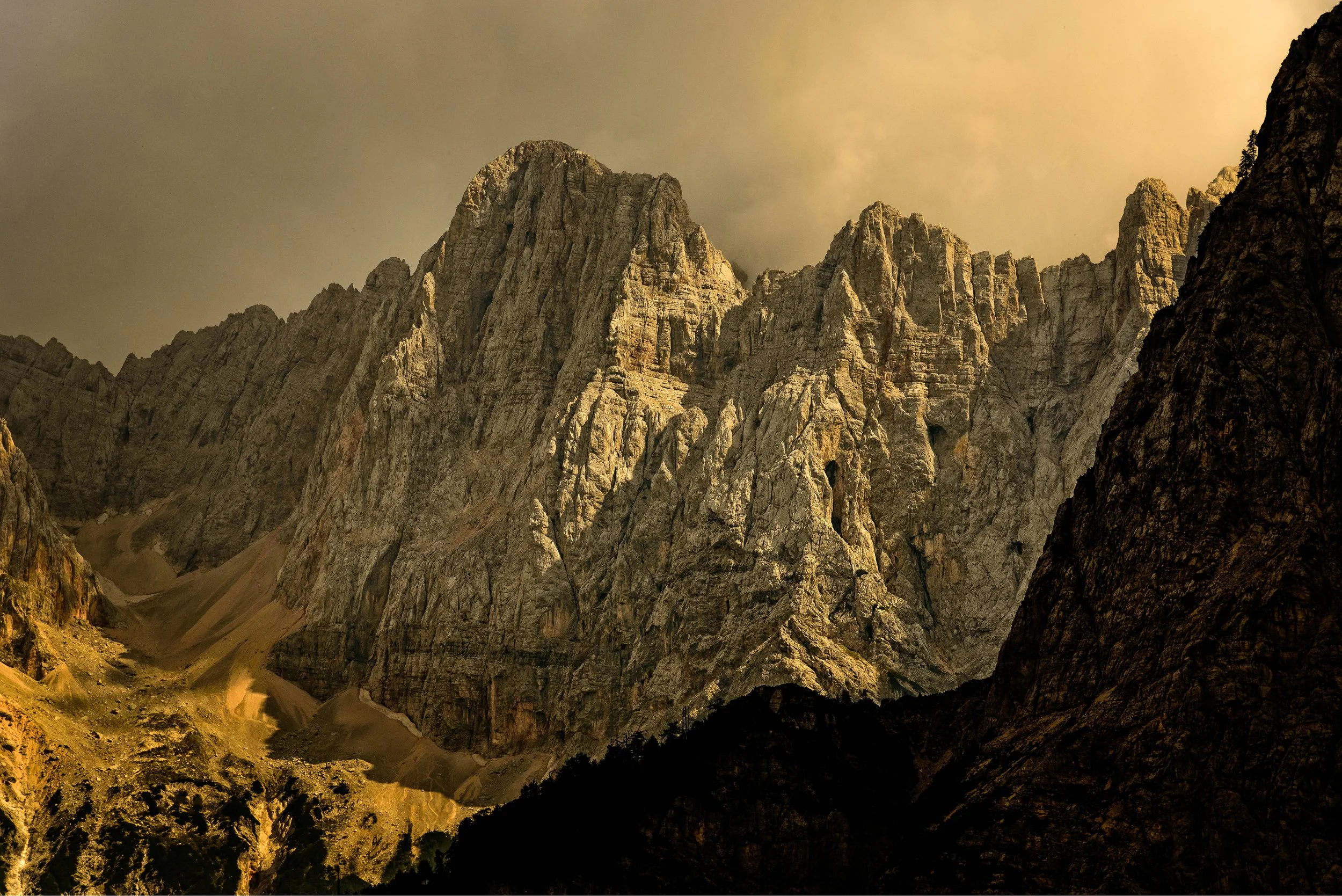 Majestic mountain range with steep rocky cliffs and rugged peaks, illuminated by warm sunlight.