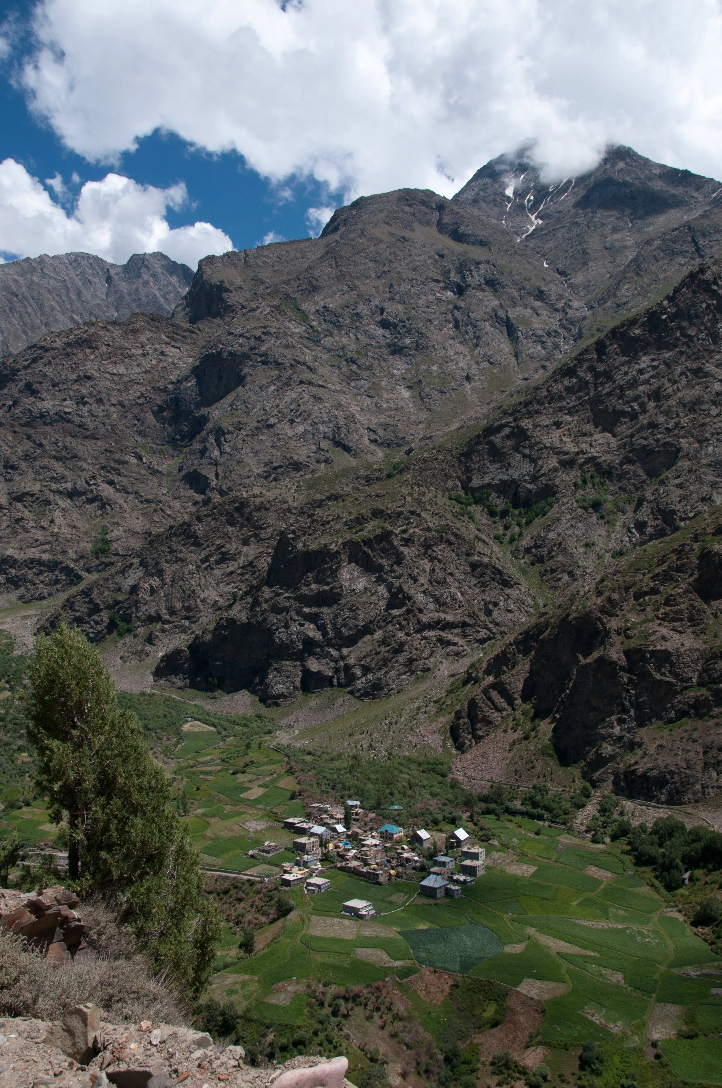 A small village surrounded by green fields and mountains under a partly cloudy sky.