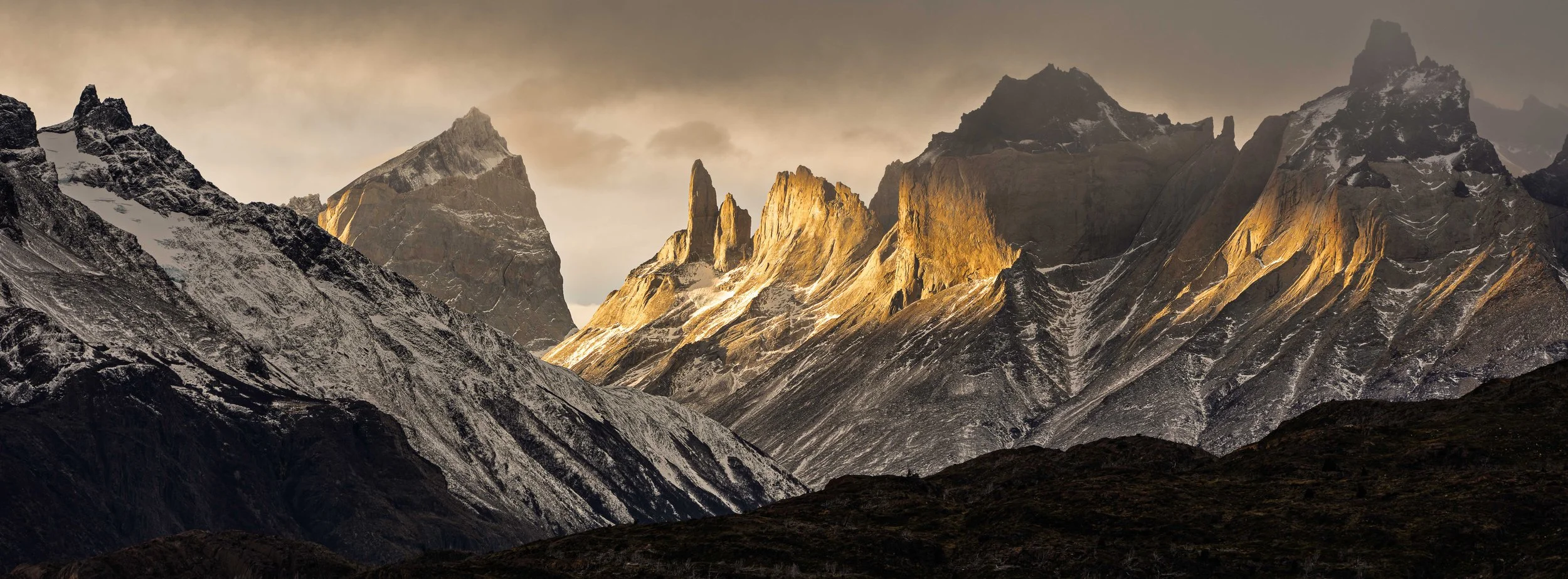 Snow-capped rugged mountain peaks at sunset with warm golden light illuminating the cliffs