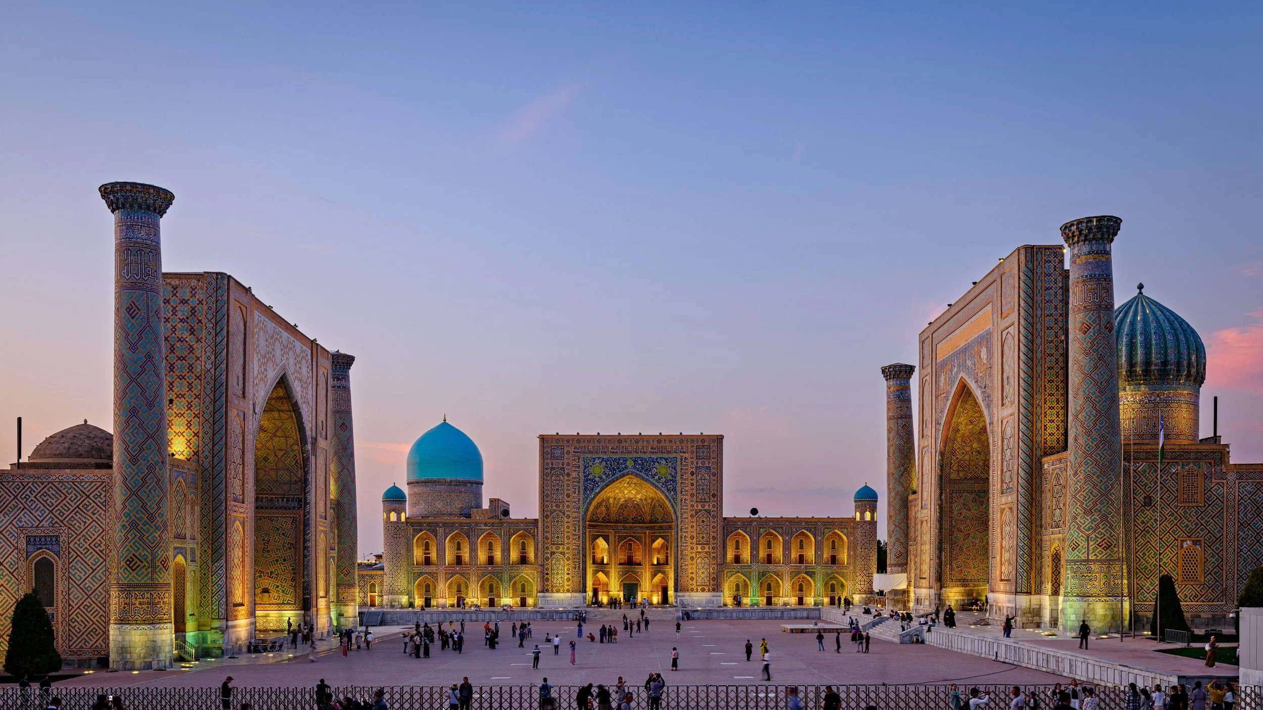 The Registan in Samarkand, Uzbekistan, with intricate Islamic architecture, colored tile mosaics, and a large open plaza at dusk.
