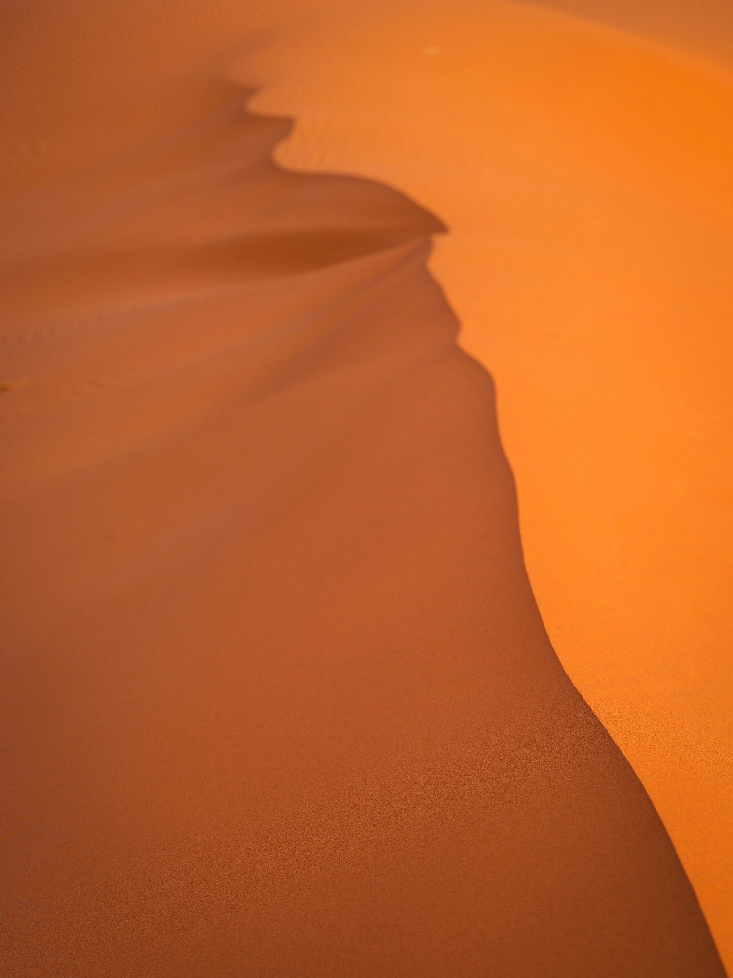 Close-up of a person’s face and hand in front of a desert sand dune during sunset.